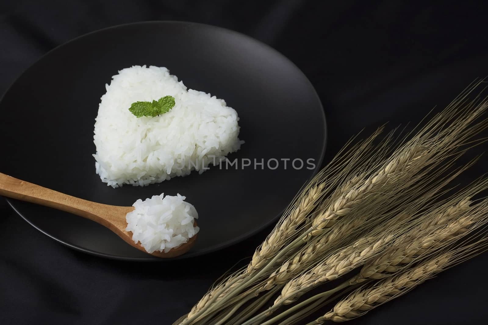 Cook rice serve with heart shape on dish decorate with ears of rice, black background.