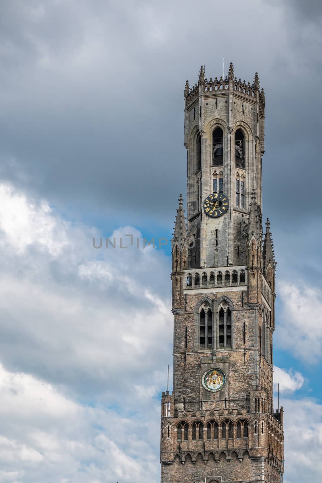 Bruges, Flanders, Belgium -  June 15, 2019: Portrait of the brown stone Halletoren building, named Belfort or Belfry, and closeup ofclock tower against gray cloudscape.