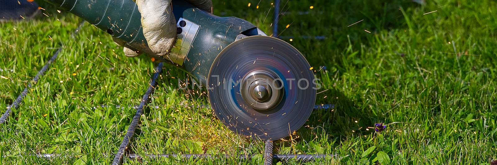 Cutting metal net with grinder on green grass. Sparks from contact materials. Worker outside, cut the steel net. Process with angle grinder