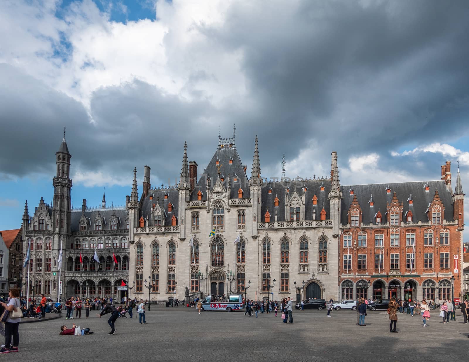 Bruges, Flanders, Belgium -  June 15, 2019: Facades of NE side of Markt square under heavy cloudscape. People in front. Buildings include Provincial Court in center and Historium on left.