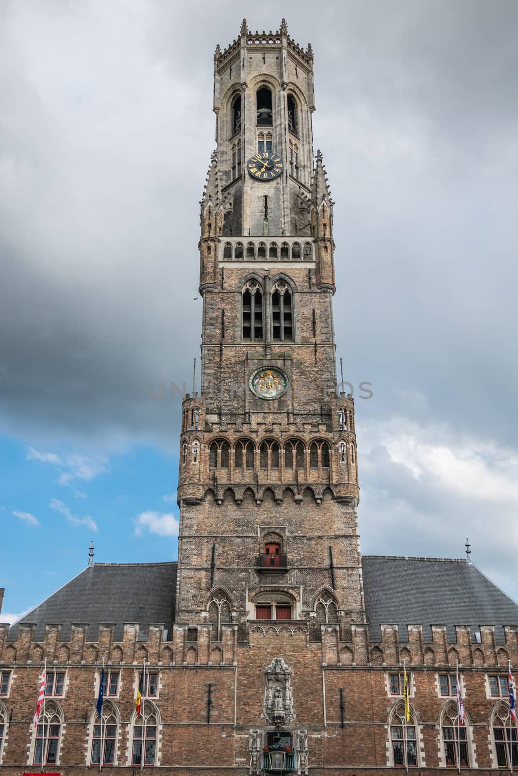Bruges, Flanders, Belgium -  June 15, 2019: Frontal view on the brown stone Halletoren building, named Belfort or Belfry, against gray cloudscape.