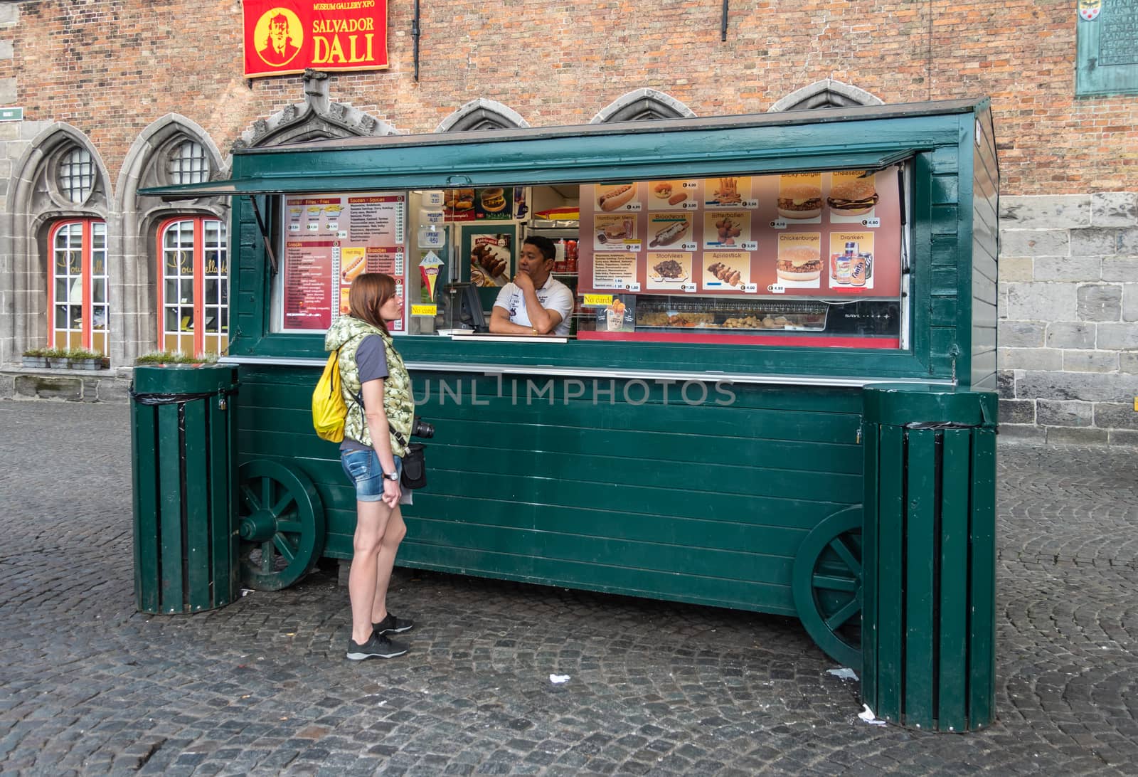 Bruges, Flanders, Belgium -  June 15, 2019: Green wooden inconic French Fries booth in front of Belfry. Vendor and customer. Red banner for Dali exhibition.