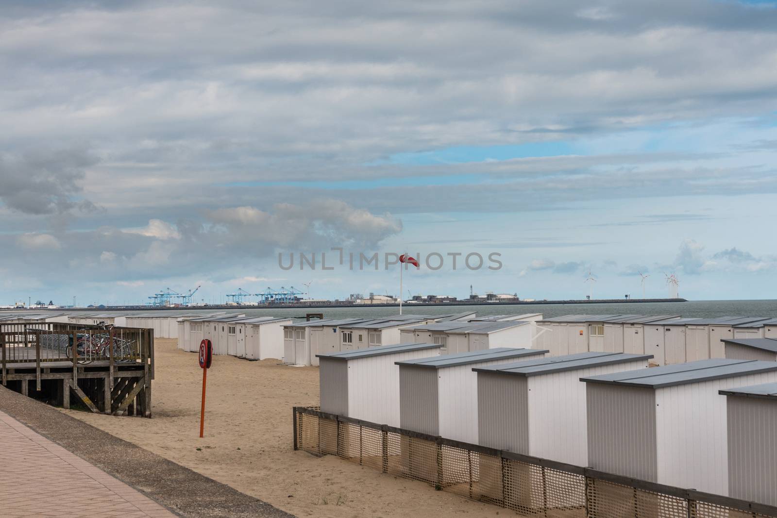 Knokke-Heist, Flanders, Belgium -  June 16, 2019: Knokke-Zoute part of town. Rows of white beach cabins on the sand with Zeebrugge LNG-sea terminal in back under pastel cloudscape.
