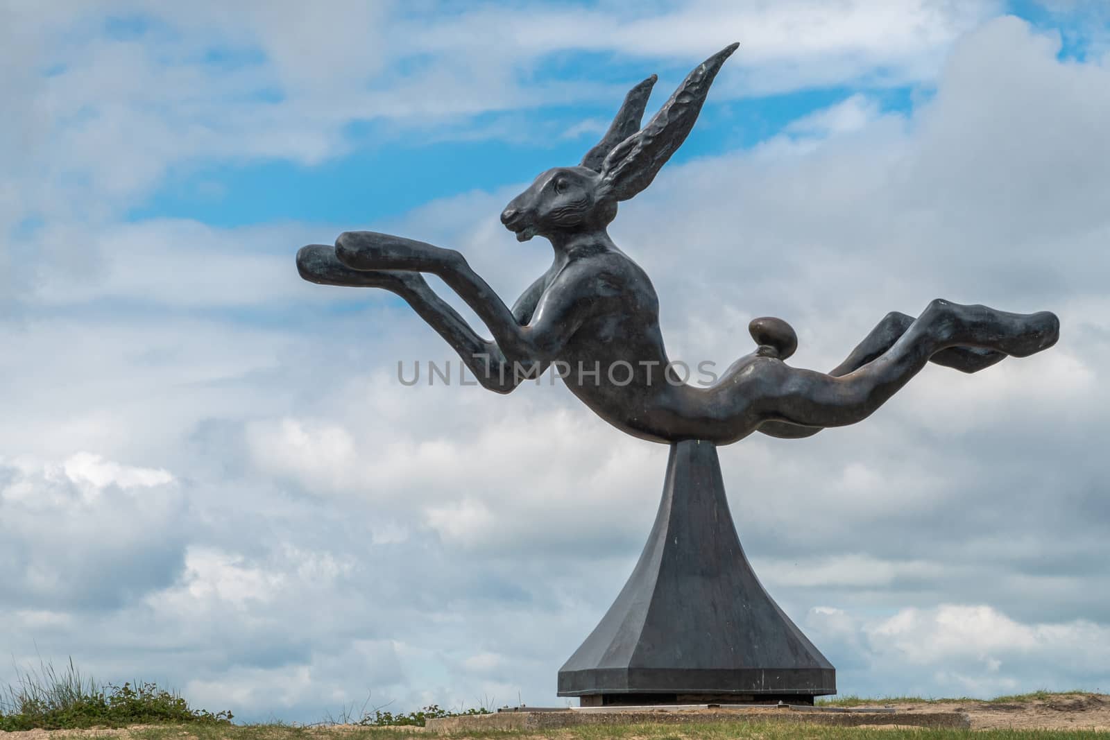 Knokke-Heist, Flanders, Belgium -  June 16, 2019: Knokke-Zoute part of town. Closeup of hare statue at end of boardwalk. Dunes of Zwin and white on blue cloudscape.