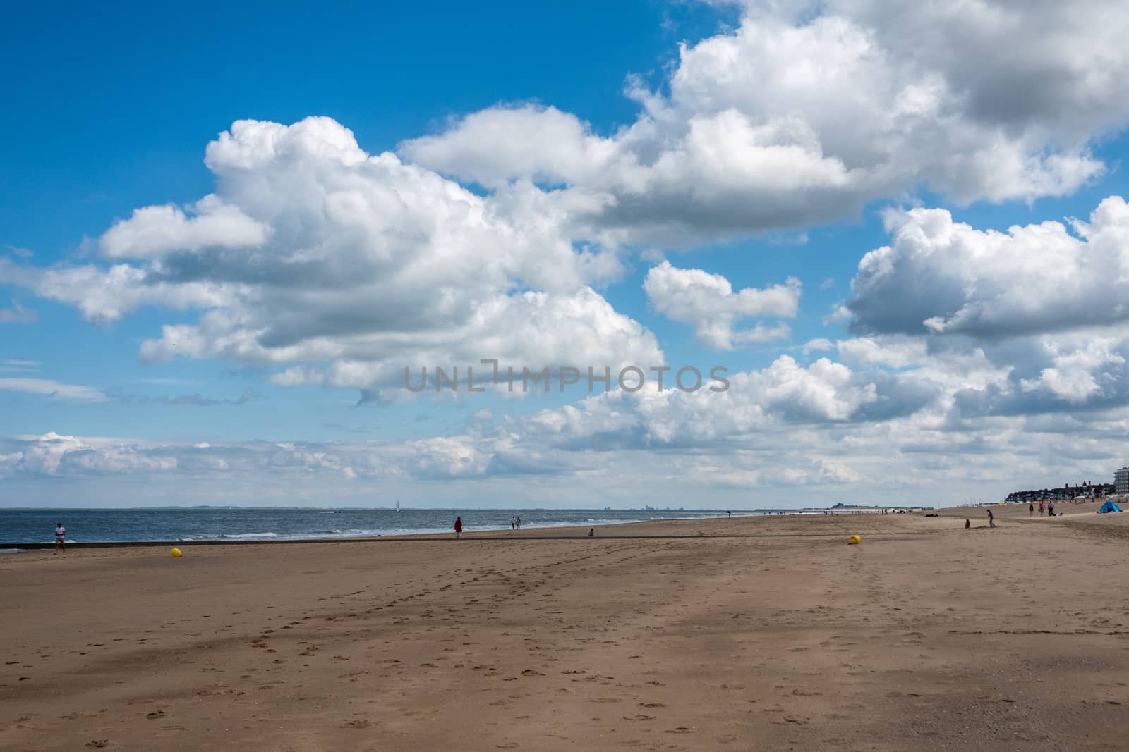 Knokke-Heist, Flanders, Belgium -  June 16, 2019: Knokke-Zoute part of town. Long view over wide brown-beige sandy beach at low tide under blue sky with white cloudscape. Some people.