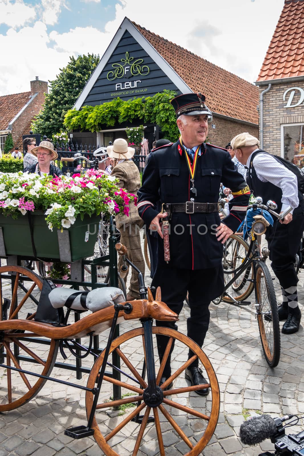 Sluis, the Netherlands -  June 16, 2019: Man dressed up as Belgian Gendarme of a century ago, with historic wooden bike and a saucisse as weapon. Other people and facades in back.