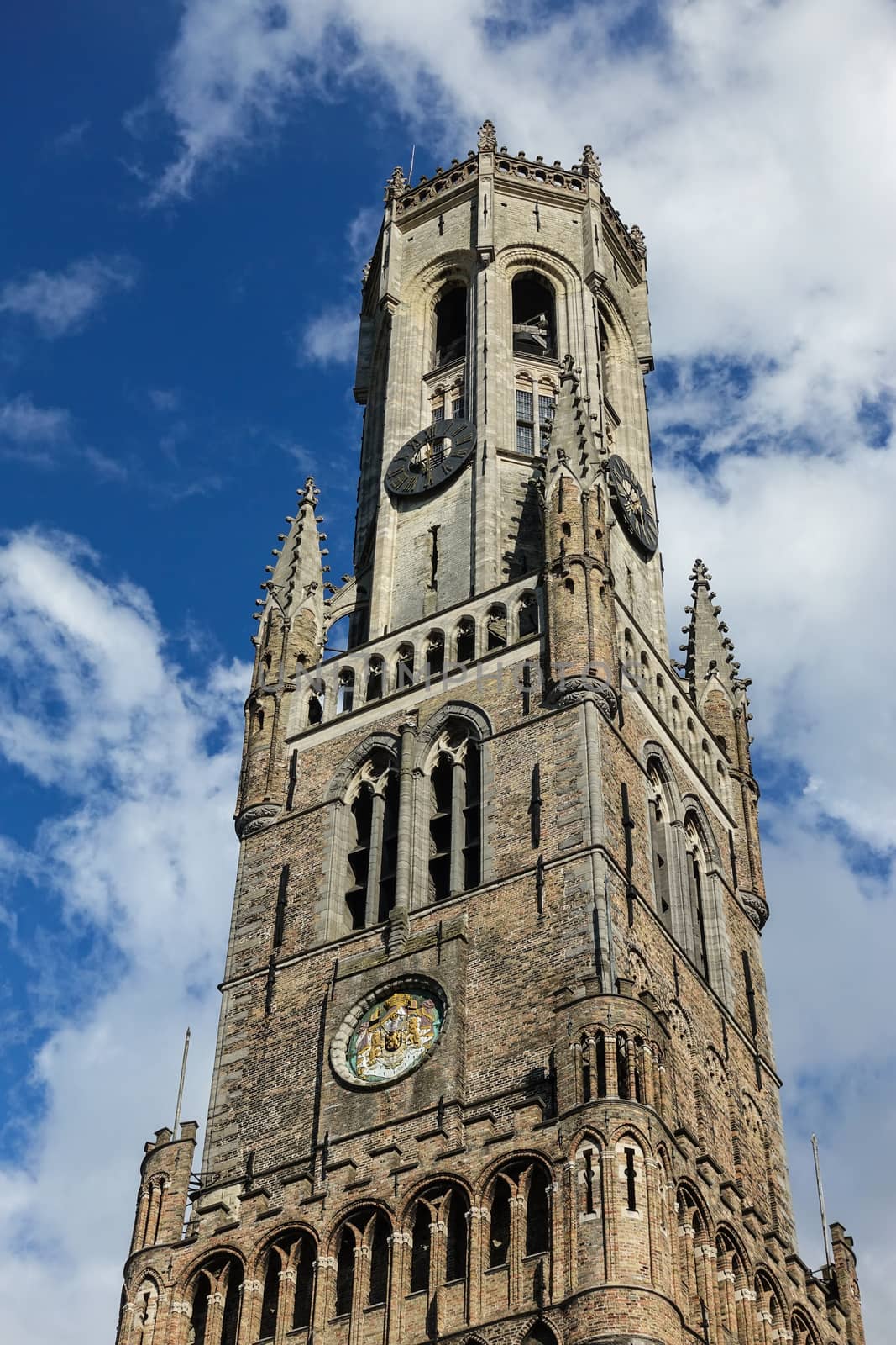 Bruges, Flanders, Belgium -  June 16, 2019: Brown-gray Brick stone Top of the tower of the Belfry against blue sky with white clouds.