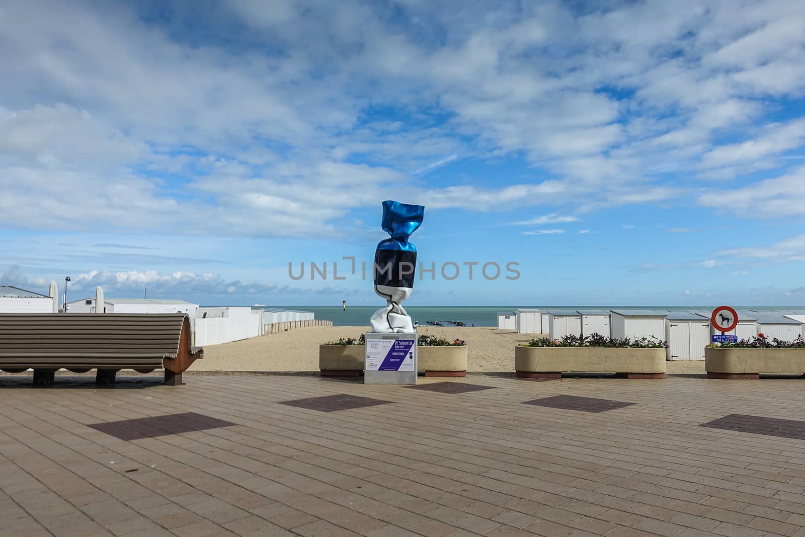 Knokke-Heist, Flanders, Belgium -  June 16, 2019: Knokke-Zoute part of town. Statue of wrapped candy standing on pedestal adjacent to beach. Rows of white cabins. Cloudscape.