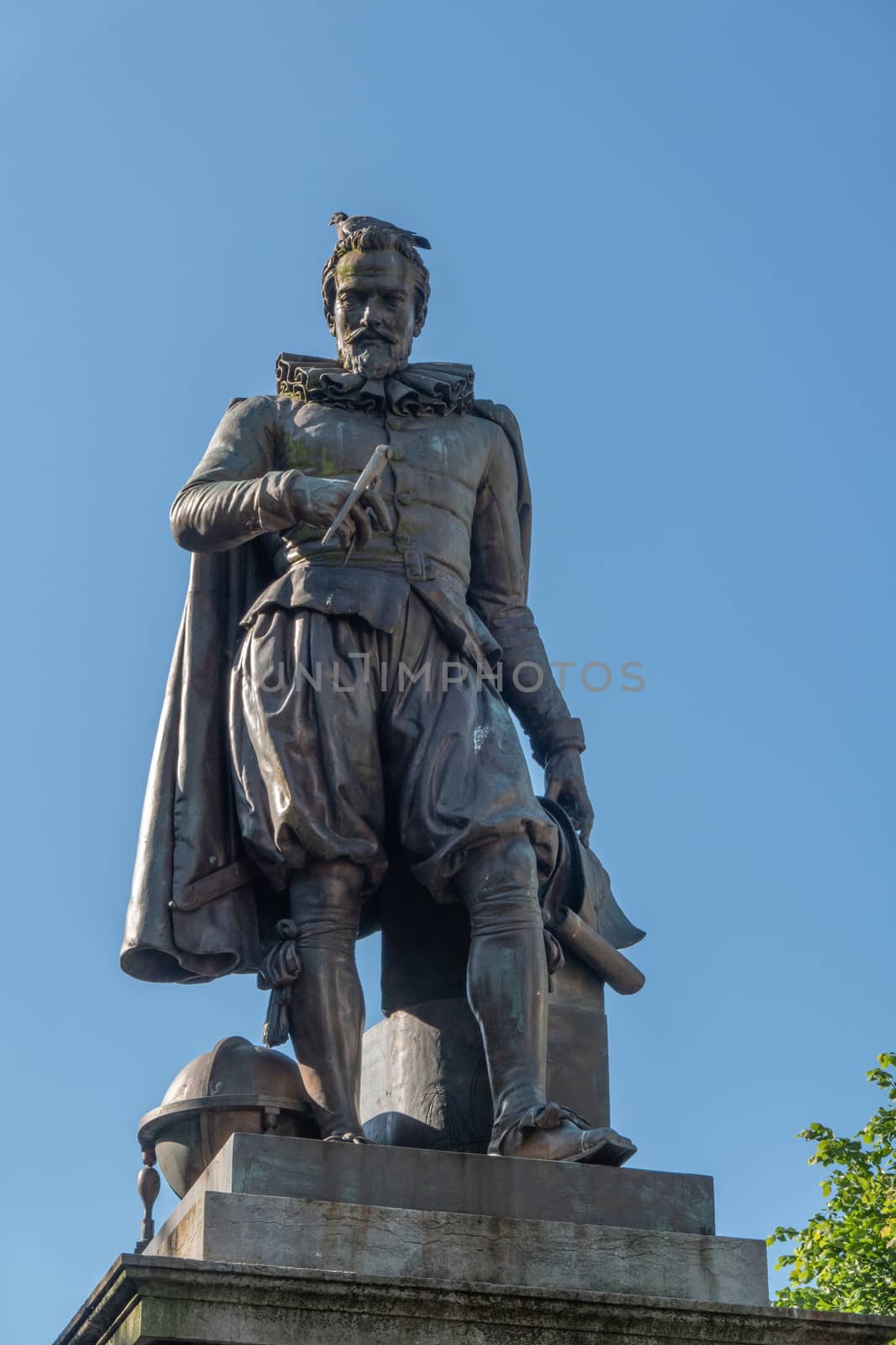 Bruges, Flanders, Belgium -  June 17, 2019: Closeup of Simon Stevin statue under blue sky. Some green foliage. Pigeon on his head.