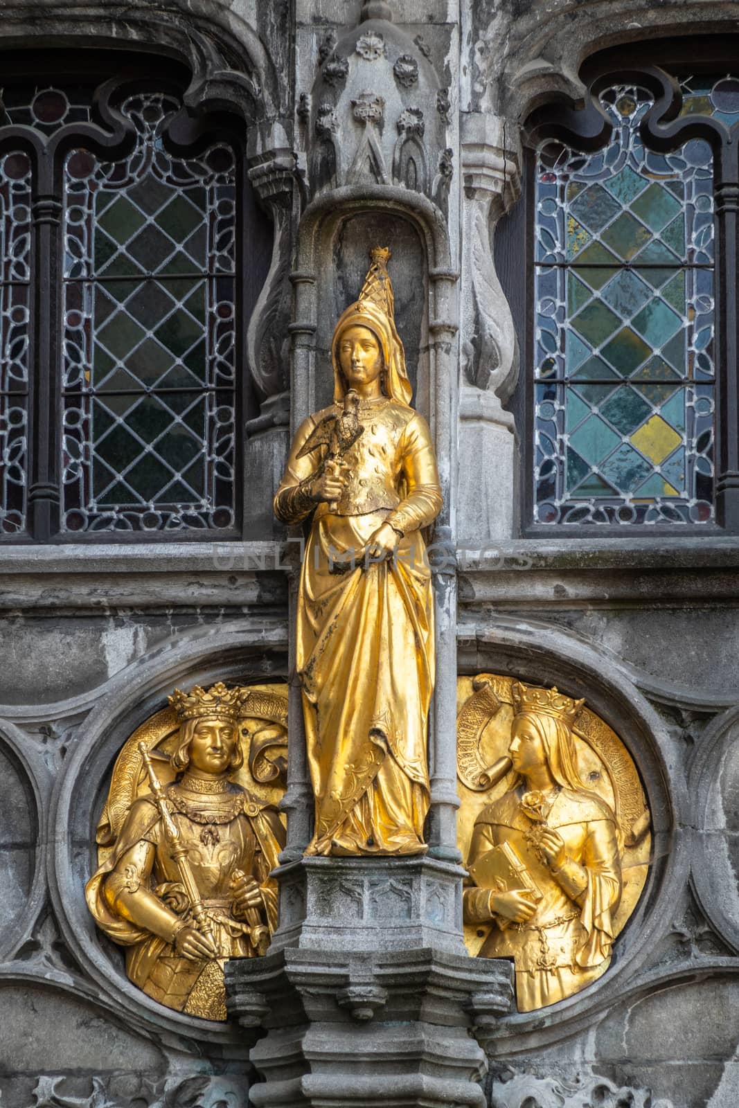 Bruges, Flanders, Belgium -  June 17, 2019: Detail with golden Noblity statues of facade of Basilica of the Holy Blood on the Burg square. Set in dark gray stone facade with stained windows.