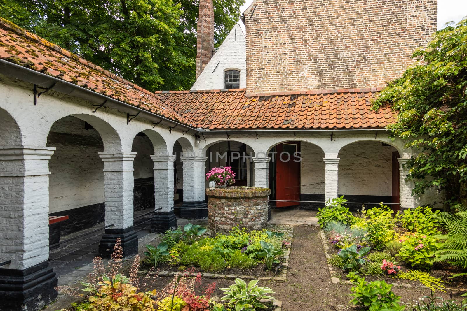 Bruges, Flanders, Belgium -  June 17, 2019: Enclosed herb garden of house in beguinage, Lots of greens, some pinks, white walls and pillars, brick stone structure.