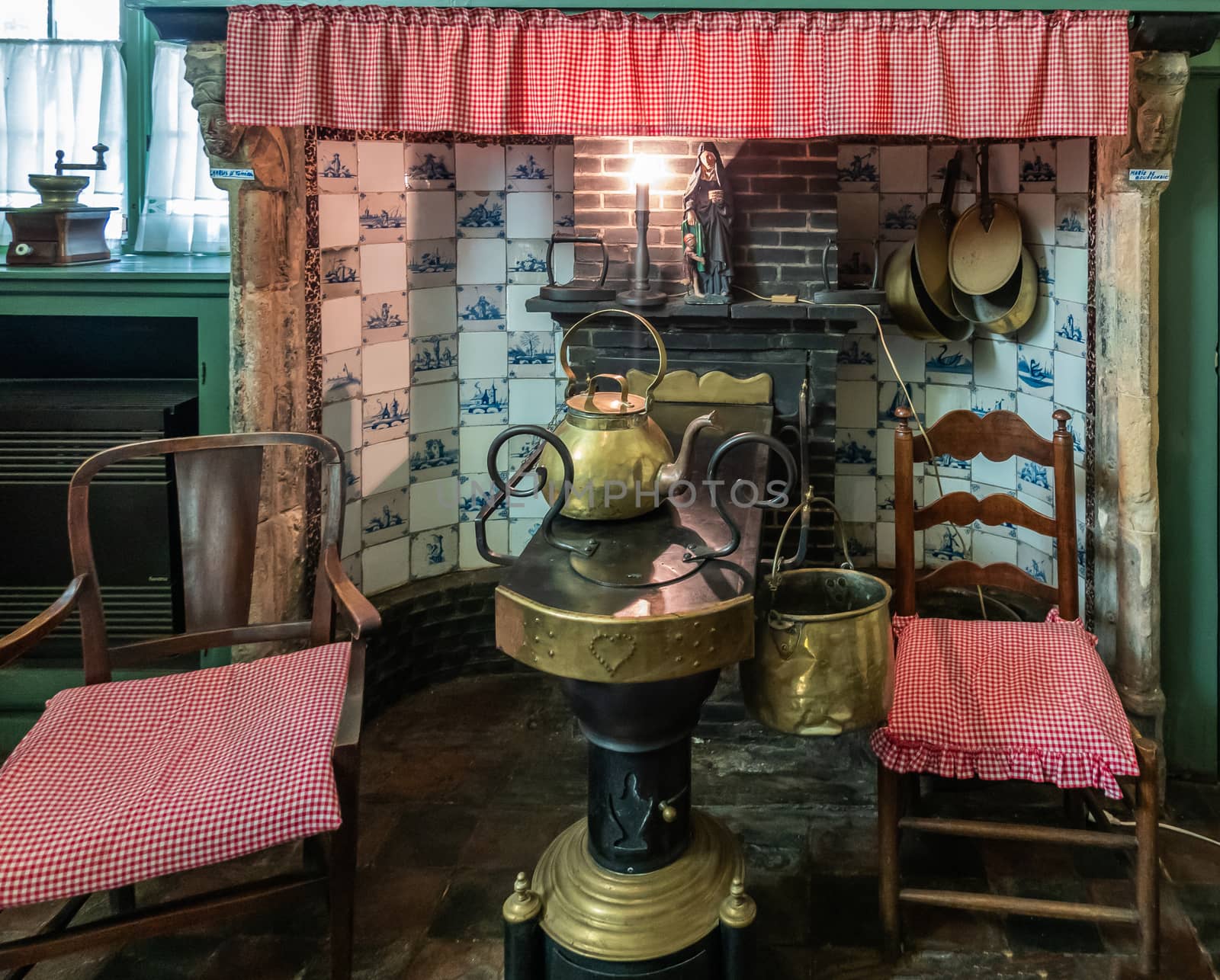 Bruges, Flanders, Belgium -  June 17, 2019: Kitchen of house in beguinage comes with hearth, long Leuvense Stove, chairs, coffee grinder, religious art, and pottery. Delfts Blue tiles.