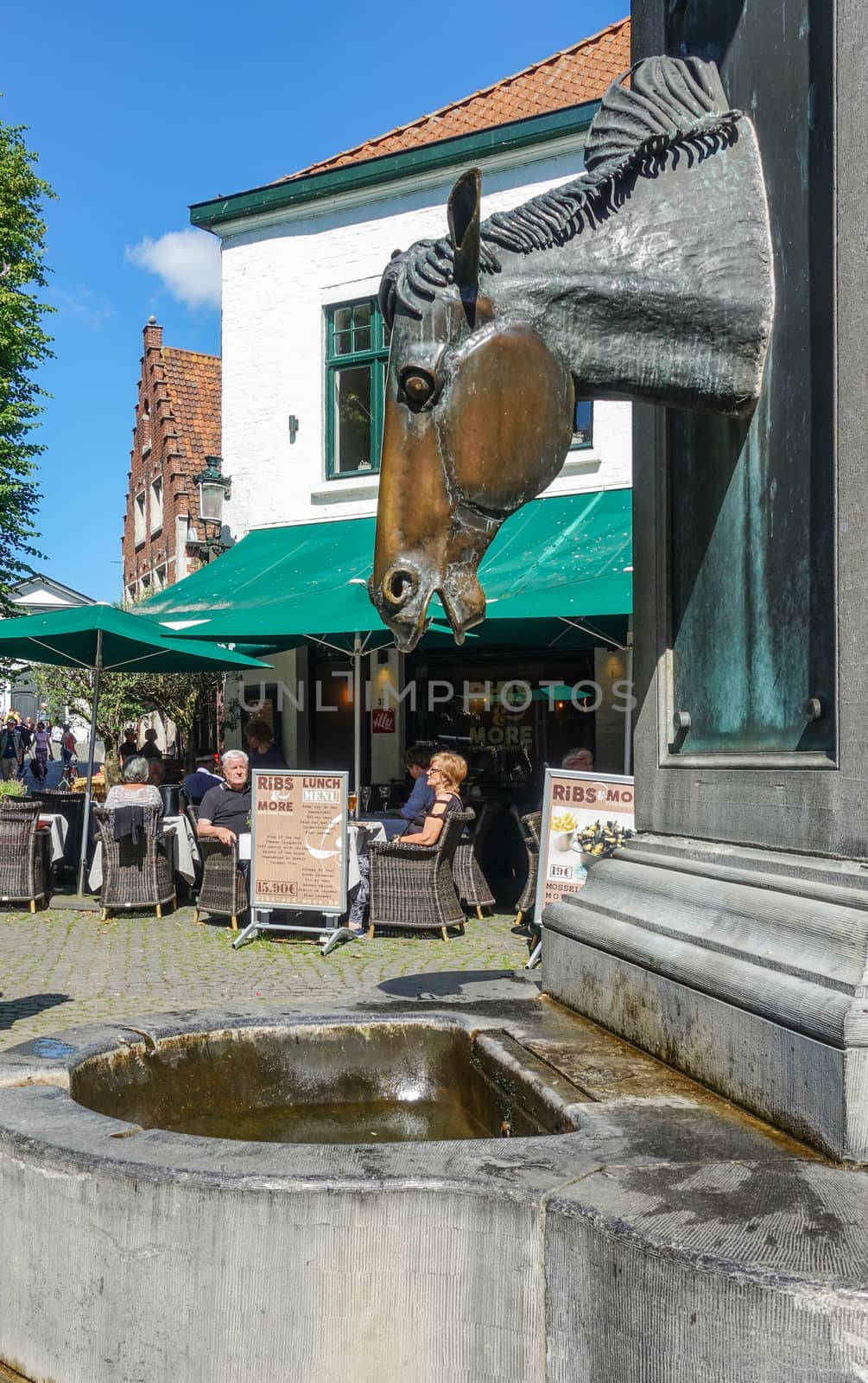 Bruges, Flanders, Belgium -  June 17, 2019: Gray stone water pump with horse head as faucet especially for horses of carriages near beguinage. People eating in restaurant.