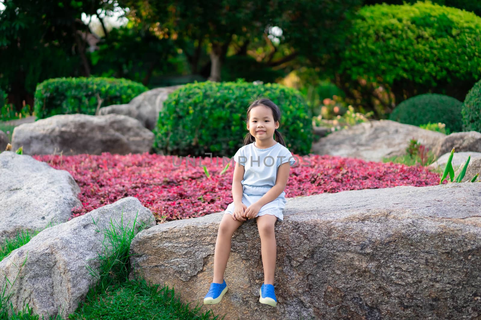 cute little girl sitting on large rock in the park