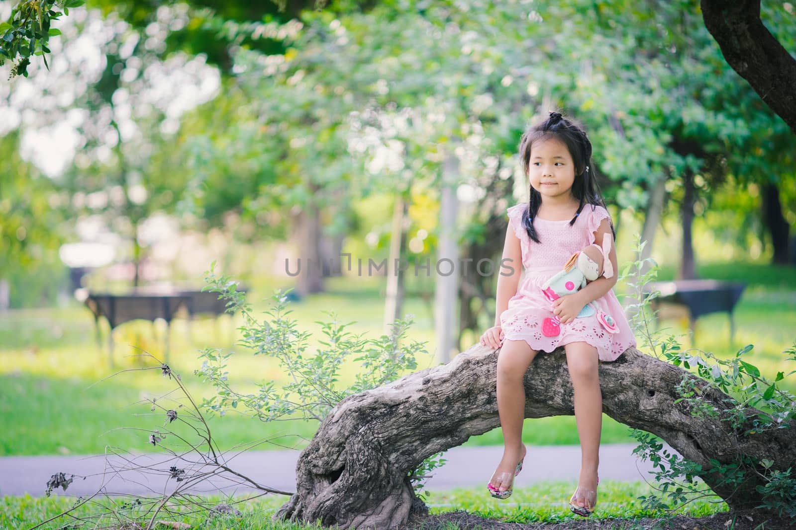 Cute little asian girl with a doll sitting in the park