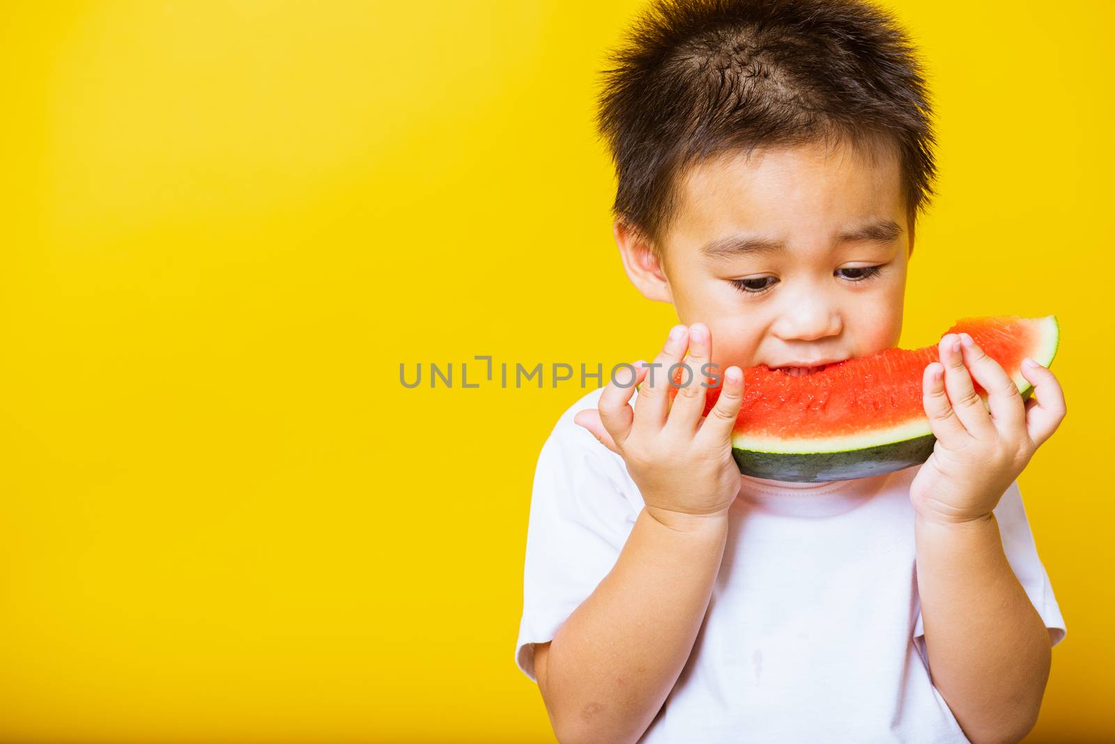 Happy portrait Asian child or kid cute little boy attractive laugh smile playing holds cut watermelon fresh for eating, studio shot isolated on yellow background, healthy food and summer concept