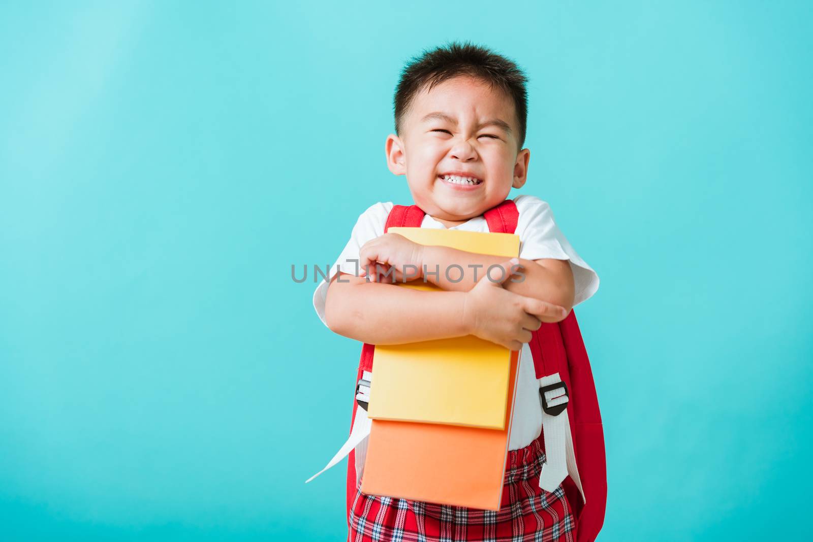 Back to school concept. Portrait Asian happy funny cute little child boy smiling and laugh hug books, studio shot isolated blue background. Kid from preschool kindergarten with school bag education