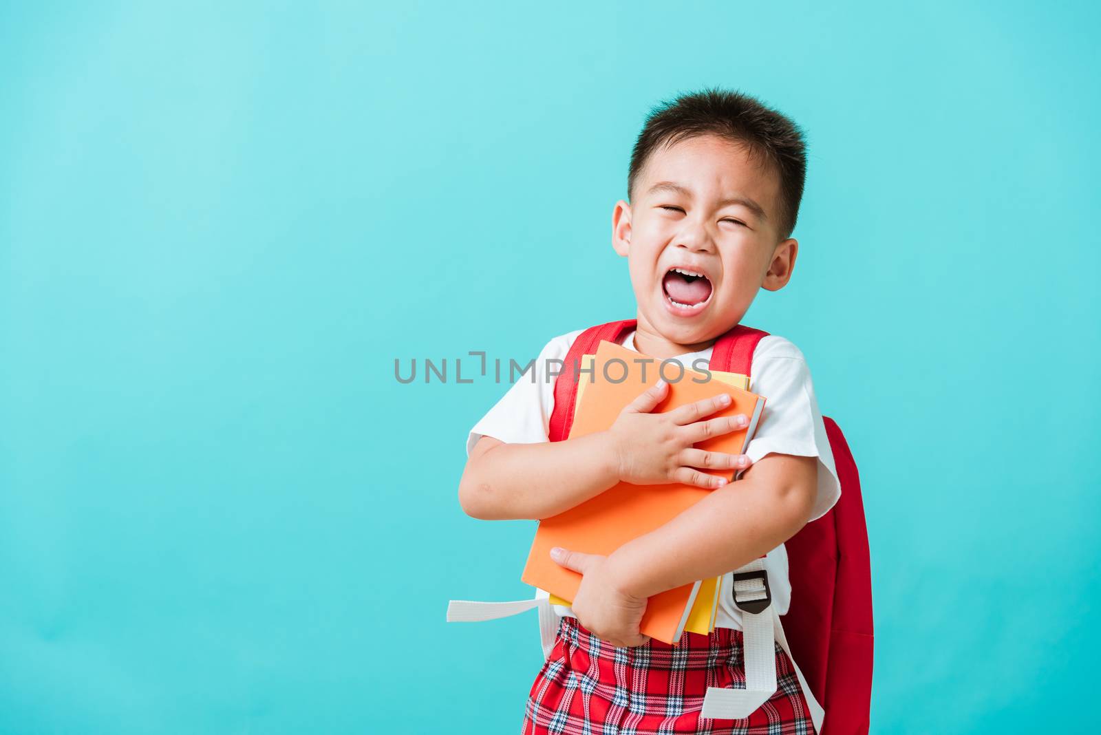 Back to school concept. Portrait Asian happy funny cute little child boy smiling and laugh hug books, studio shot isolated blue background. Kid from preschool kindergarten with school bag education