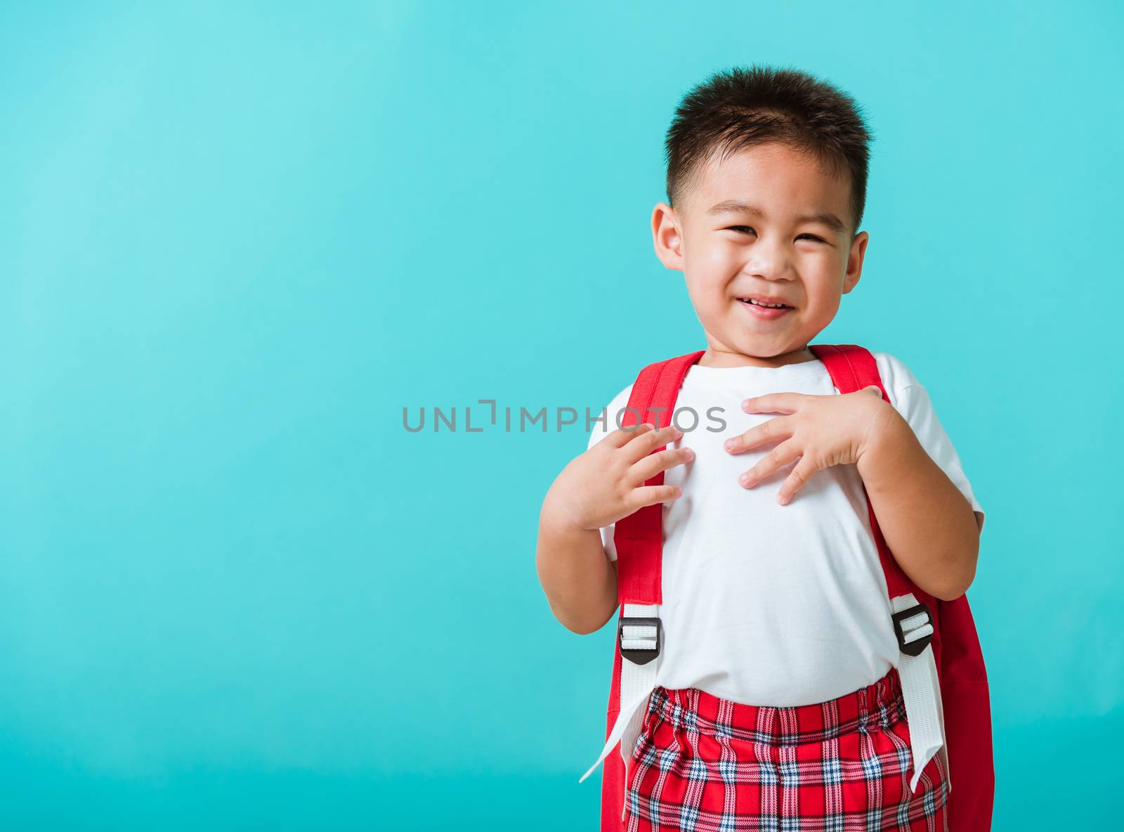 Back to school concept. Portrait closeup happy Asian cute little child boy in uniform smiling, isolated blue background. The kid from preschool kindergarten with a school bag backpack