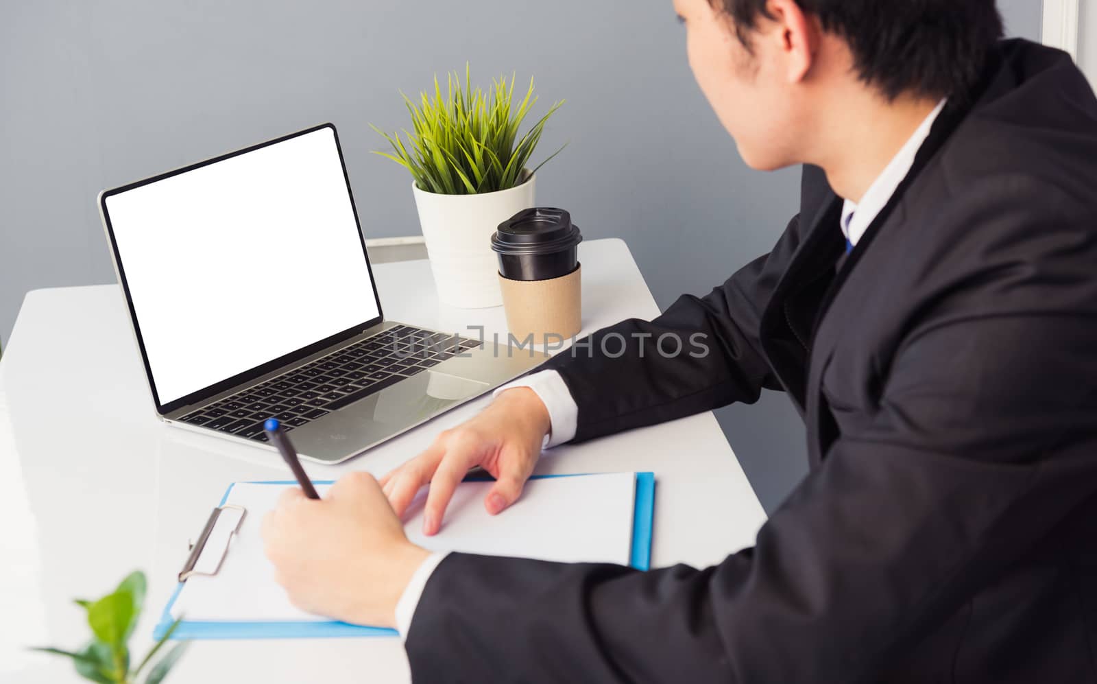 Work from home, Asian young businessman smile wearing suit video conference call or facetime by laptop computer on desk and write taking notes on paper at home office