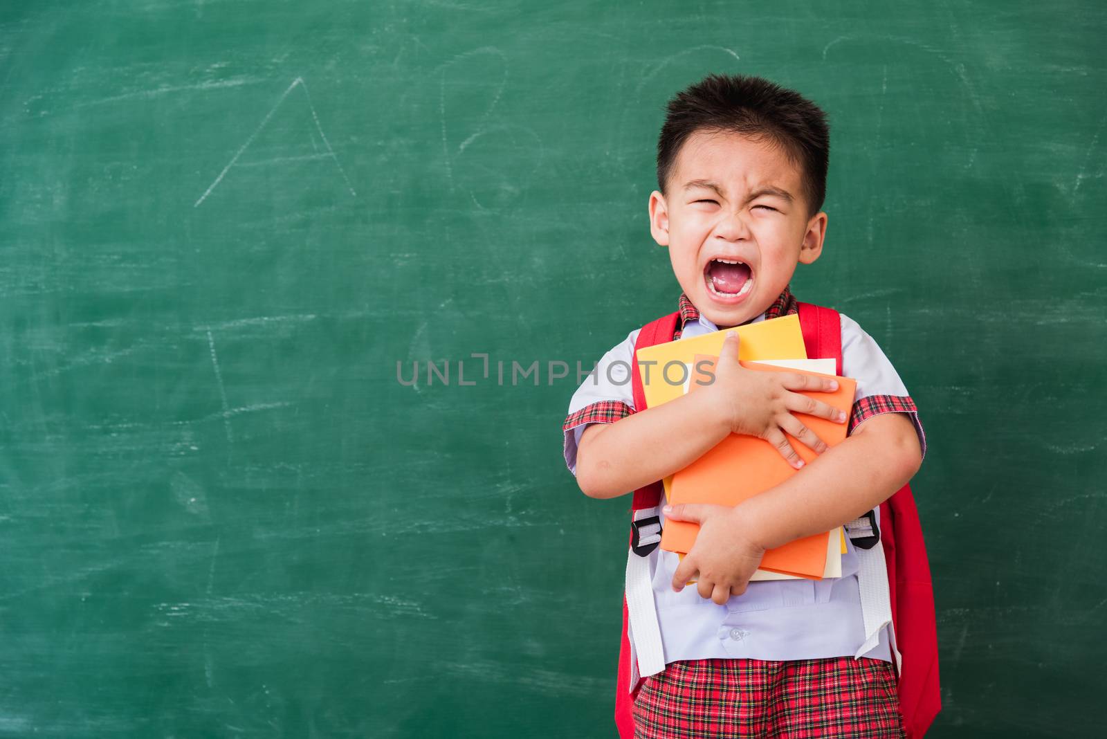 Back to School. Happy Asian funny cute little child boy from kindergarten in student uniform with school bag hold or hug books smile on green school blackboard, First time to school education concept