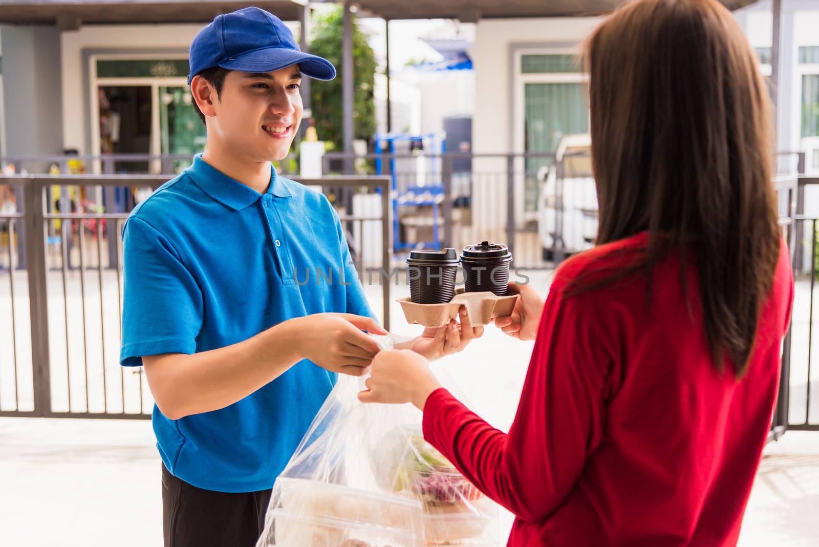 Asian young delivery man in blue uniform he making grocery service giving rice food boxes plastic bags to woman customer receiving front house under pandemic coronavirus, Back to new normal concept