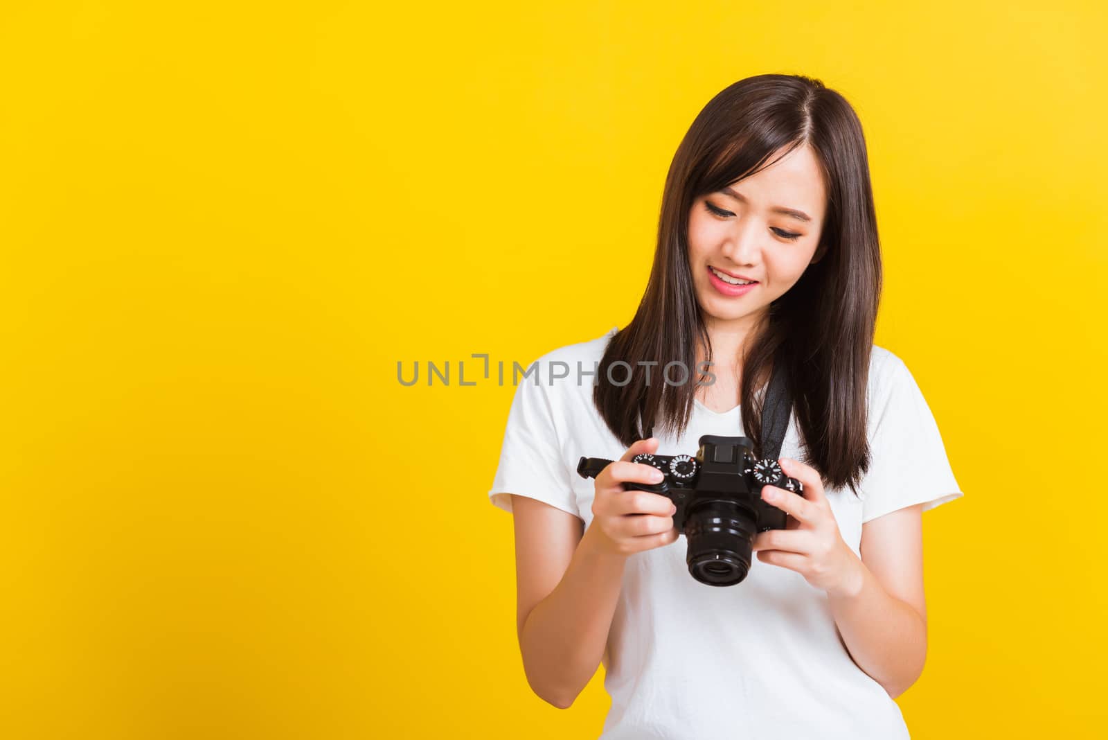 Portrait of happy Asian beautiful young woman photographer review picture she seeing a photo on the screen of digital mirrorless photo camera after photography, isolated on yellow background
