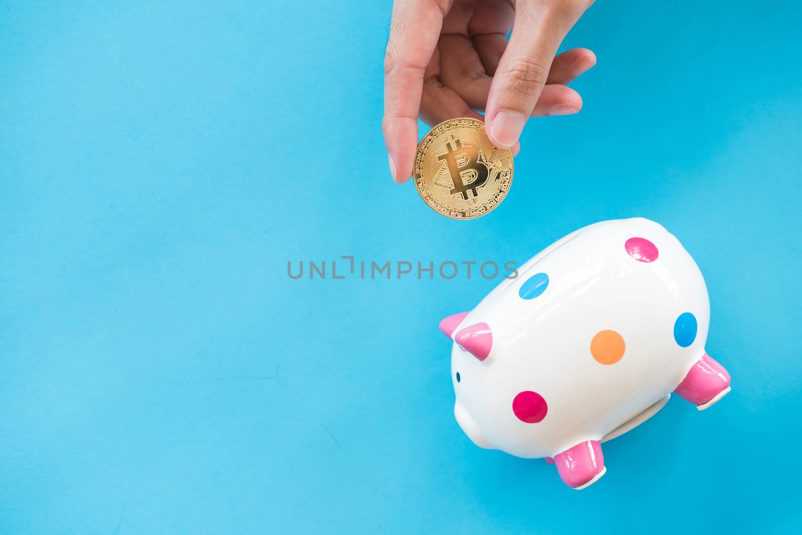 man hand put gold bitcoin into piggy bank on light blue paper background