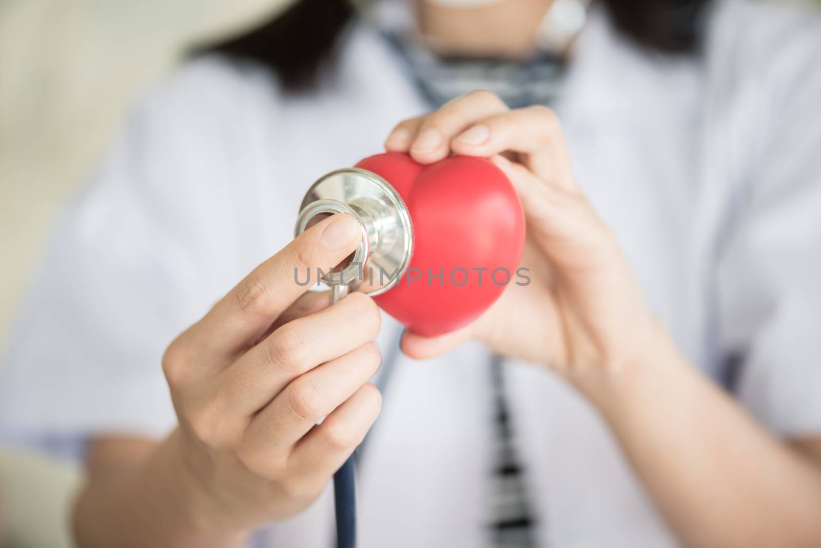 profressional woman doctor with green stethoscope checking red heart in her hand