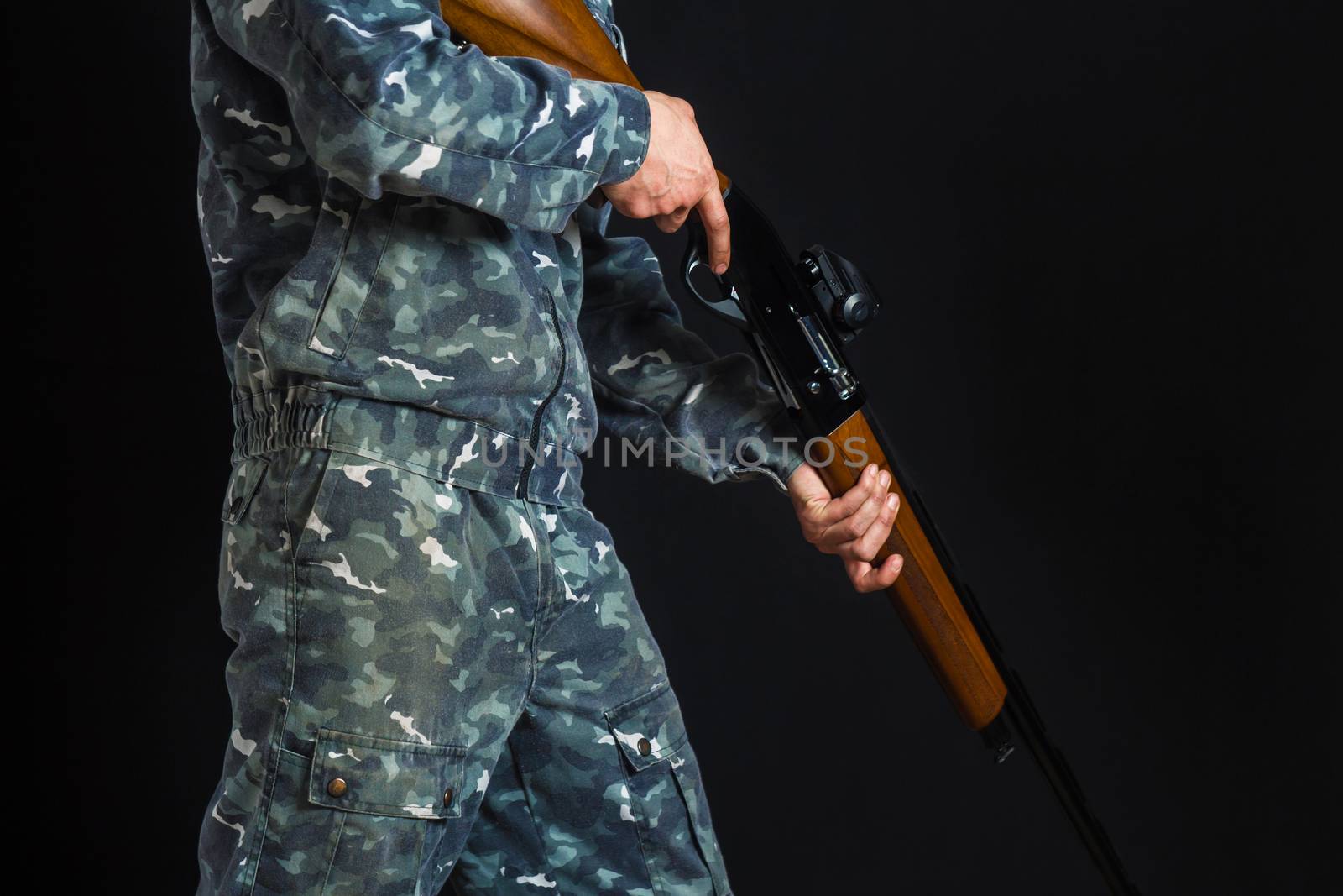 Young man with a gun. A soldier in military uniform with a shotgun. War games. Preparation for spring, autumn hunting. Soldier or hunter on a black background, isolated, copy space.