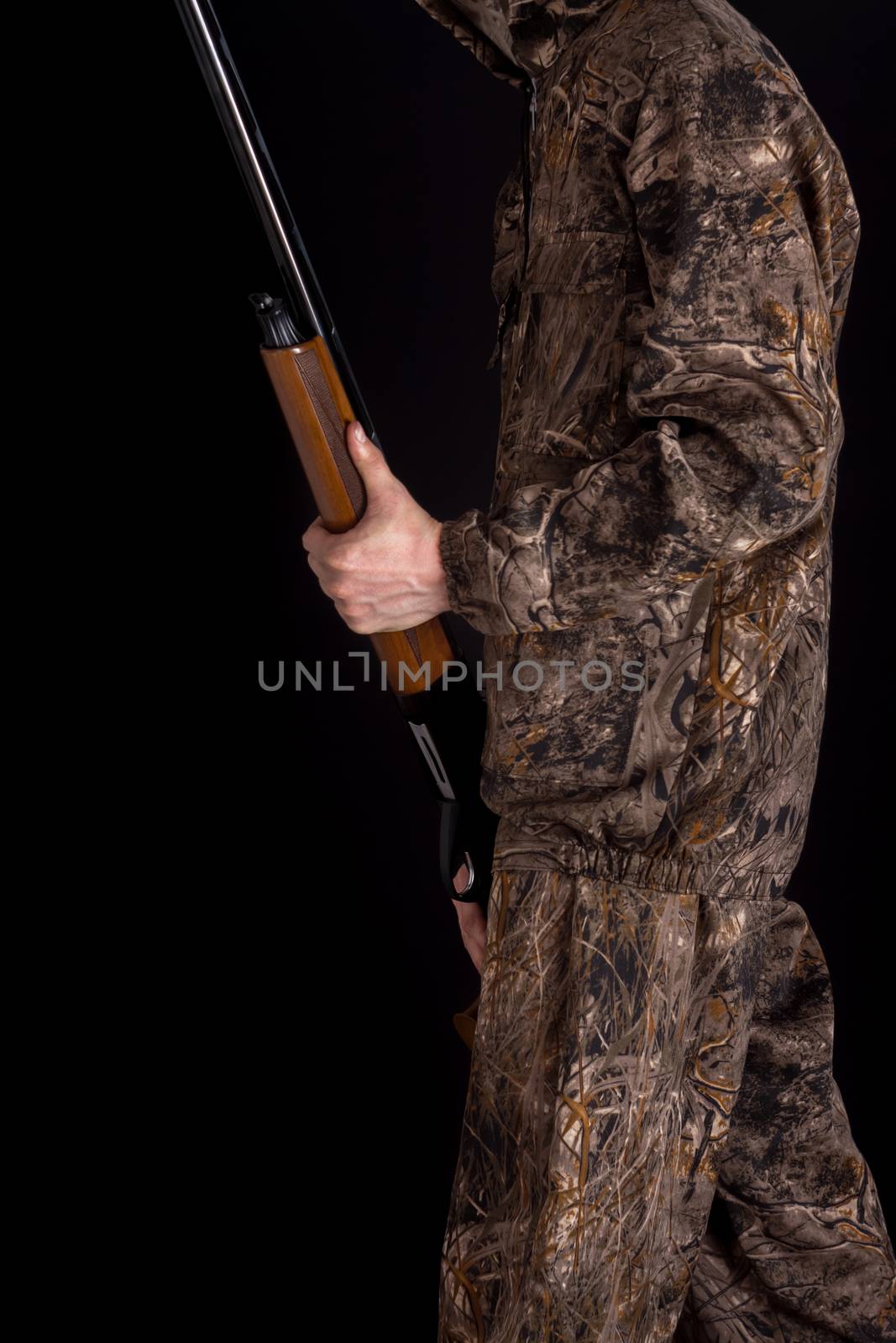 Preparation for spring or autumn hunting. Hunter in camouflage clothing with a gun on a black background isolated. The man with the shotgun. Young guy in a camo suit with a gun.