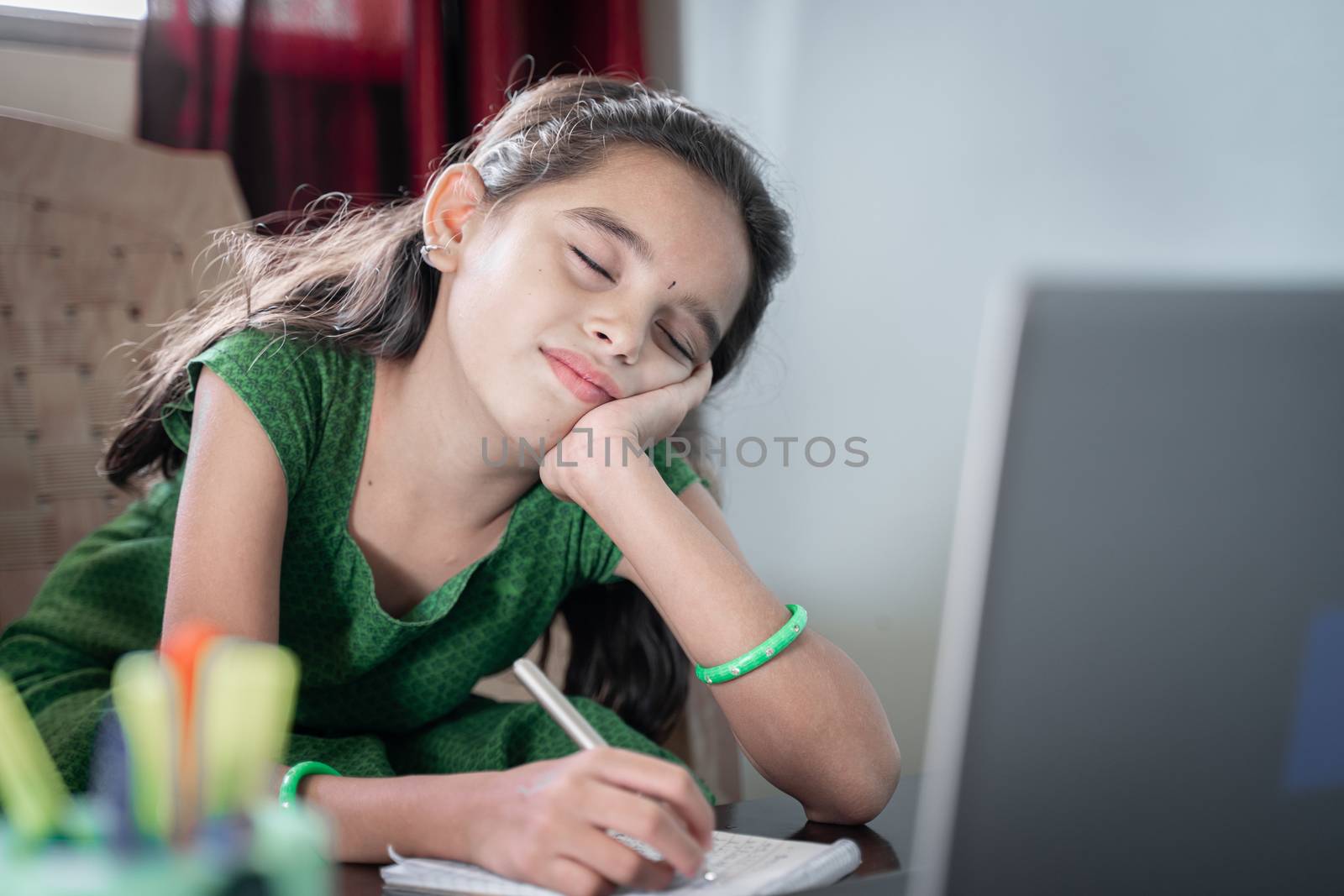 Girl child sleeping during online class infront of laptop - concept of tired kid from distance learning or online education at home during covid-19 or coronavirus lockdown