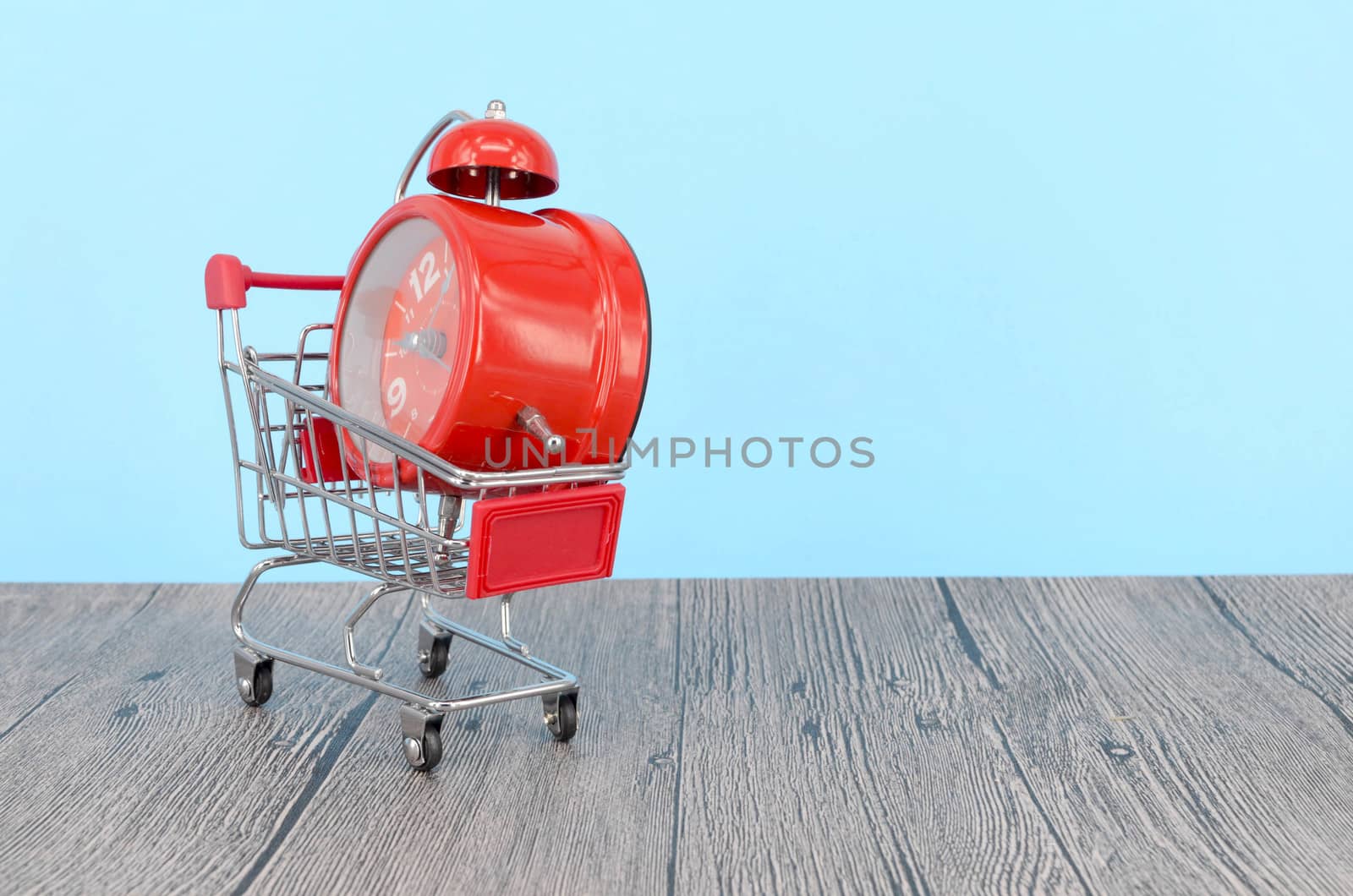 Shopping cart and classic alarm clock on wooden surface. Sale time buy mall market shop consumer concept. Selective focus.