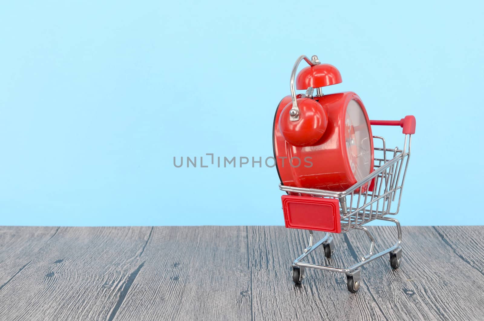 Shopping cart and classic alarm clock on wooden surface. Sale time buy mall market shop consumer concept. Selective focus.