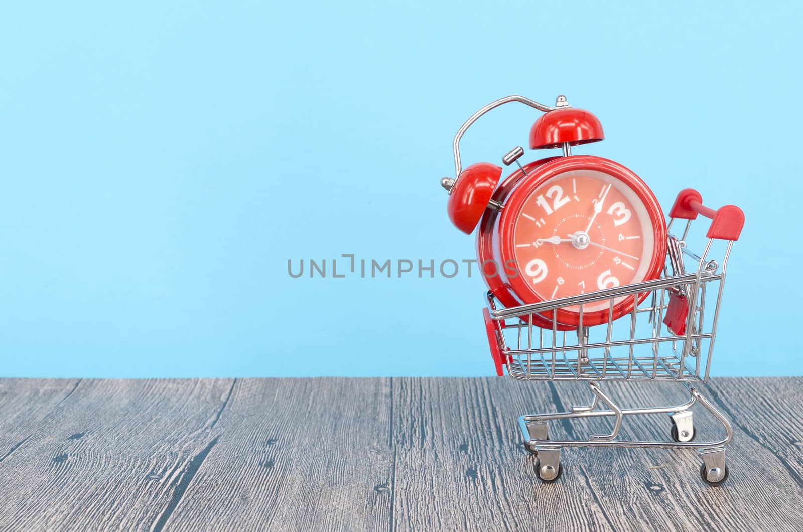 Shopping cart and classic alarm clock on wooden surface. Sale time buy mall market shop consumer concept. Selective focus.