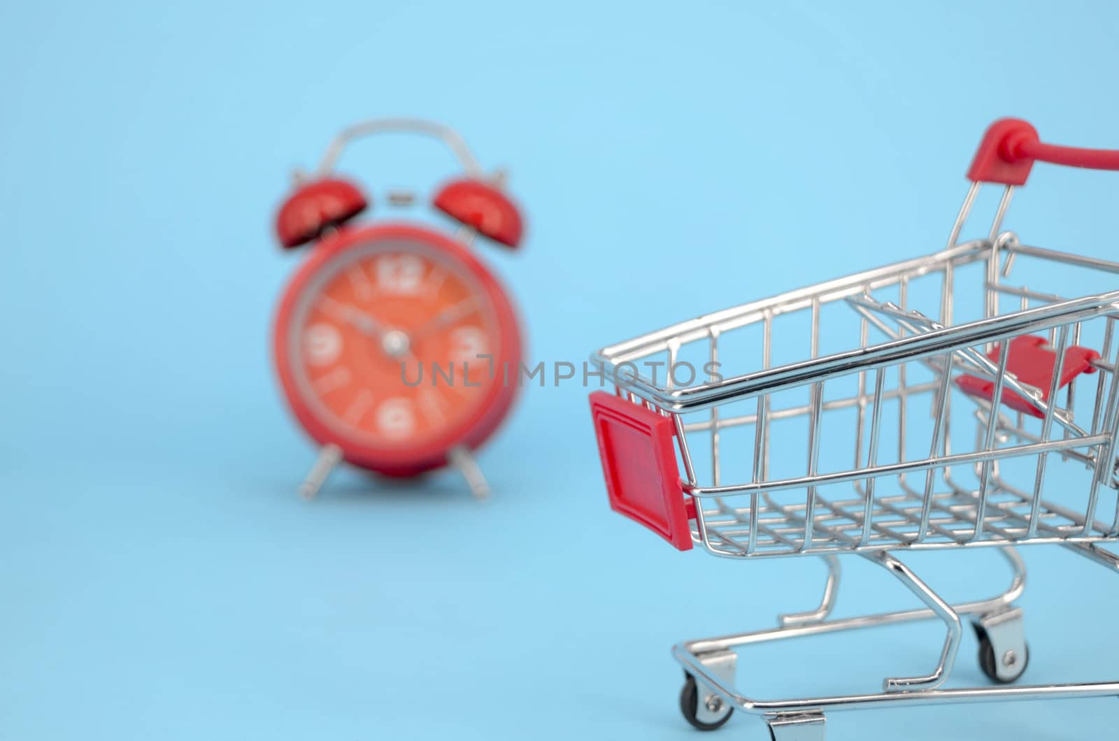 Shopping cart and classic alarm clock on blue background. Sale time market shop consumer concept. Selective focus.