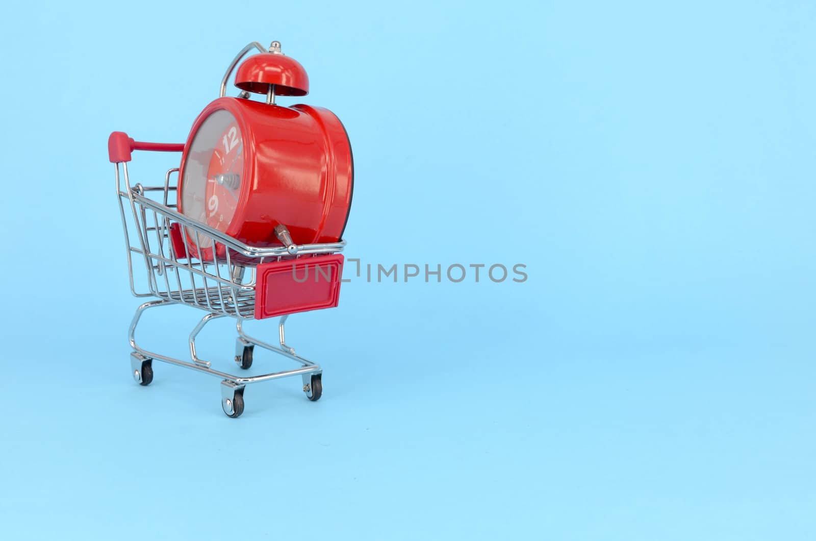 Shopping cart and classic alarm clock on blue background. Sale time market shop consumer concept. Selective focus.