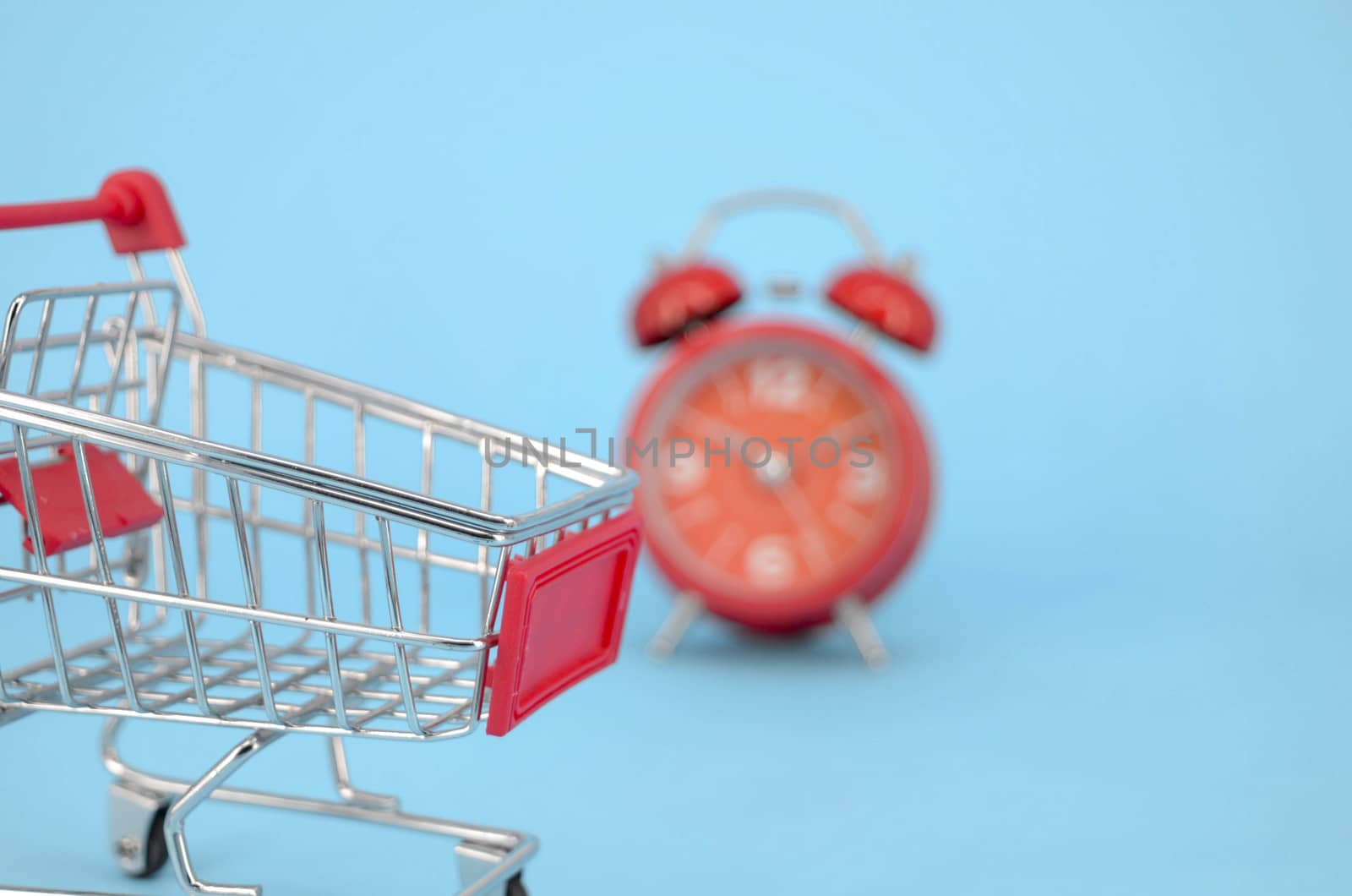 Shopping cart and classic alarm clock on blue background. Sale time market shop consumer concept. Selective focus.