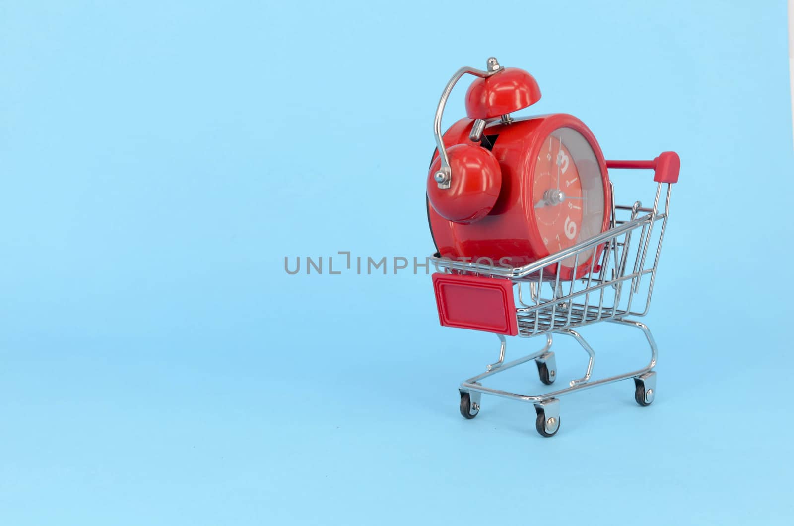 Shopping cart and classic alarm clock on blue background. Sale time market shop consumer concept. Selective focus.