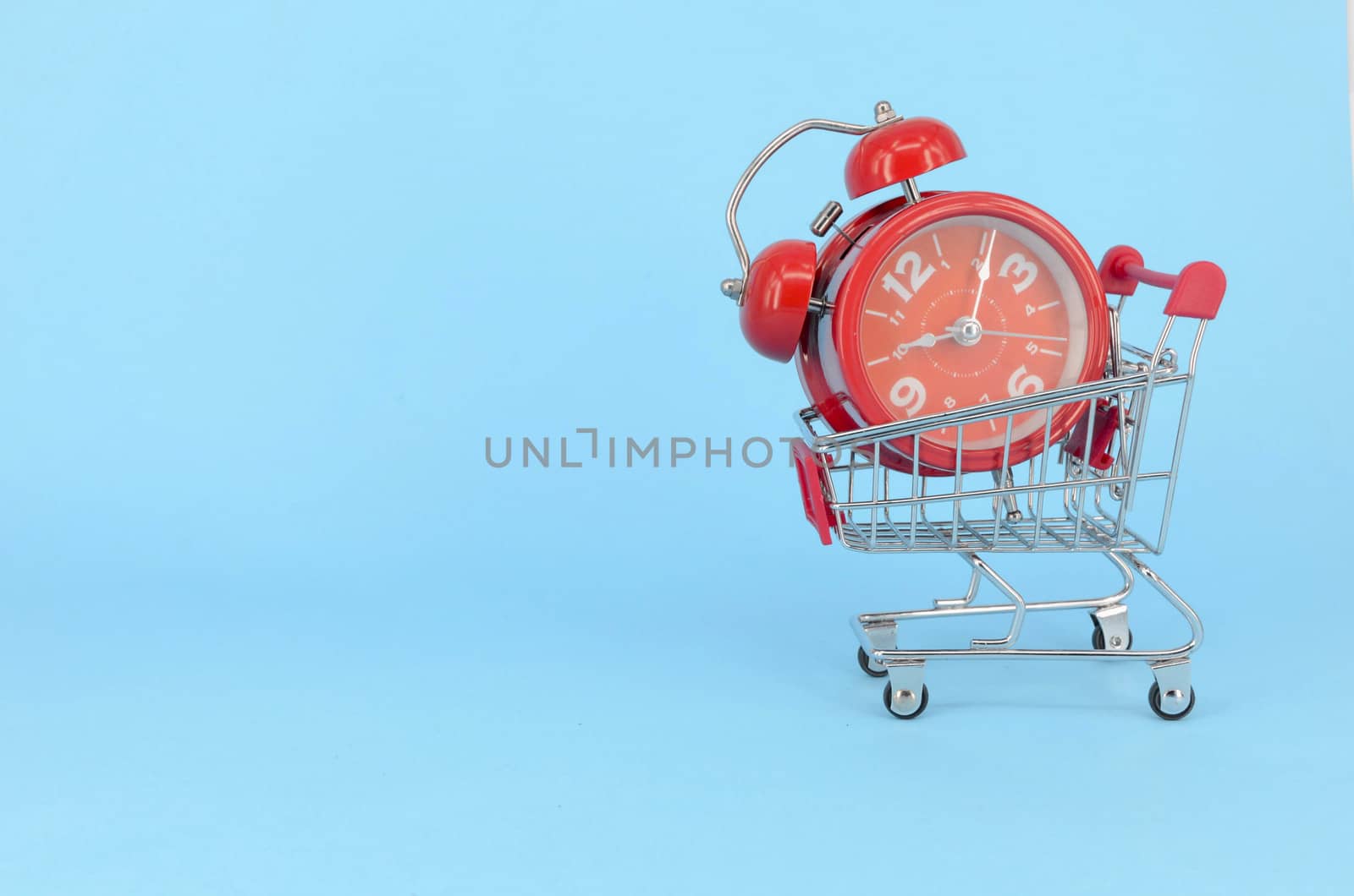 Shopping cart and classic alarm clock on blue background. Sale time market shop consumer concept. Selective focus.