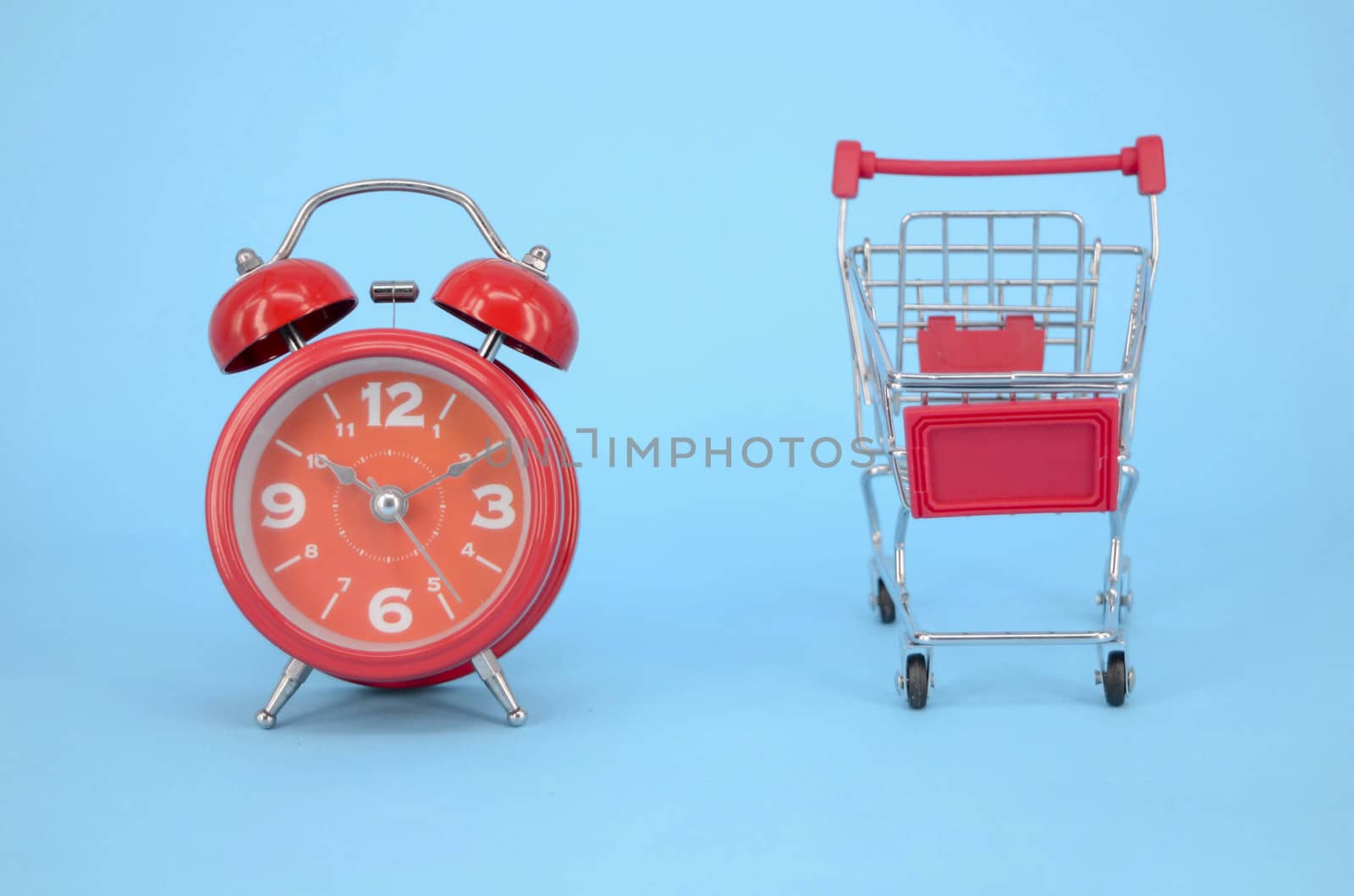 Shopping cart and classic alarm clock on blue background. Sale time market shop consumer concept. Selective focus.