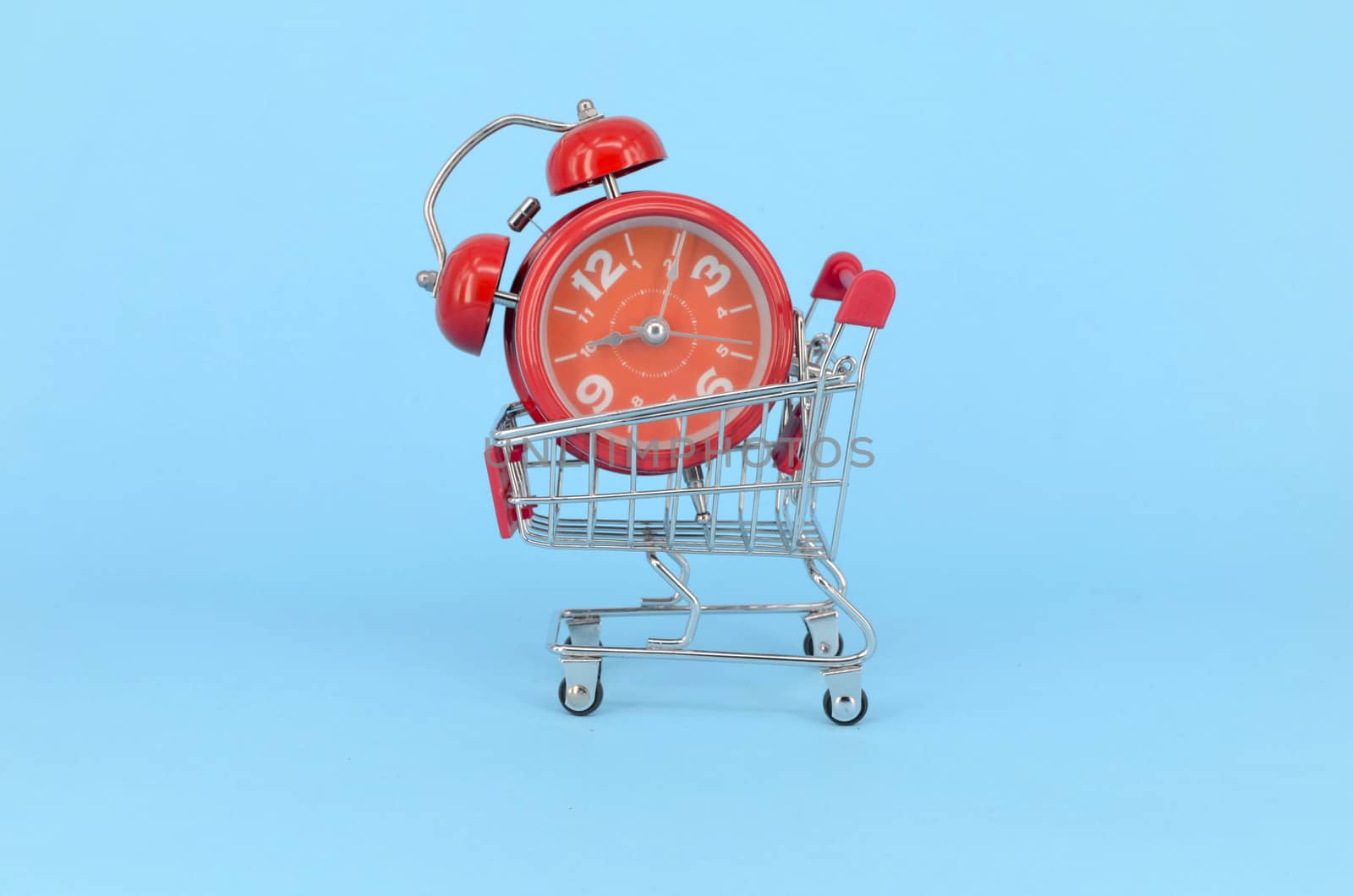 Shopping cart and classic alarm clock on blue background. Sale time market shop consumer concept. Selective focus.