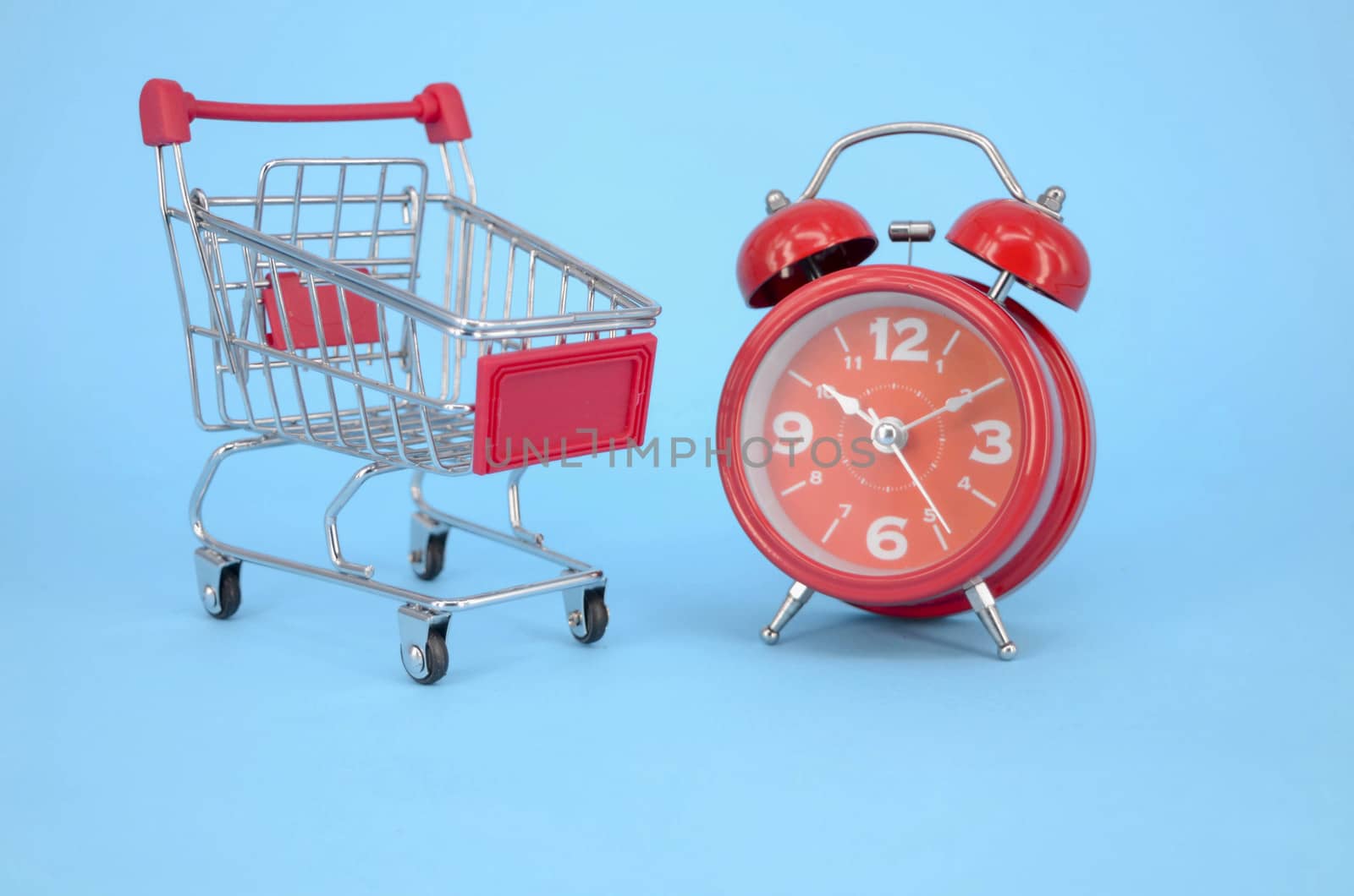 Shopping cart and classic alarm clock on blue background. Sale time market shop consumer concept. Selective focus.