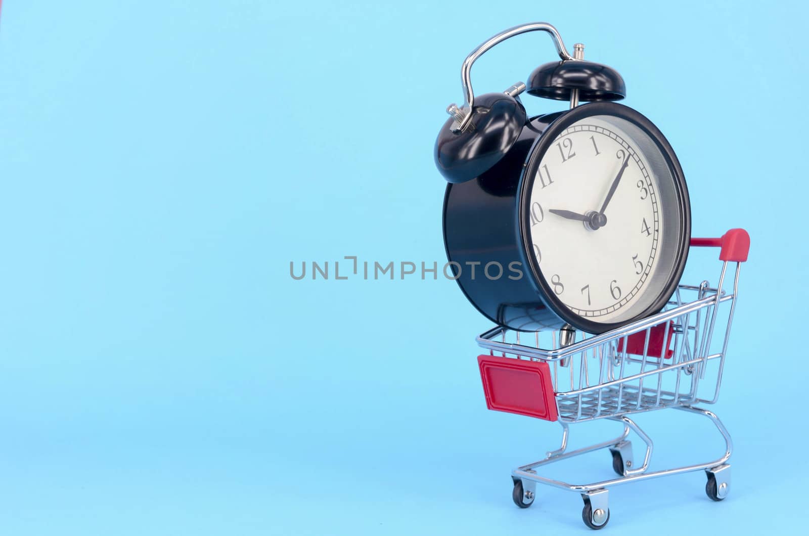 Shopping cart and classic alarm clock on blue background. Sale time market shop consumer concept. Selective focus.