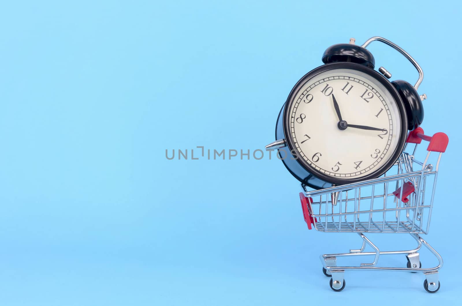 Shopping cart and classic alarm clock on blue background. Sale time market shop consumer concept. Selective focus.