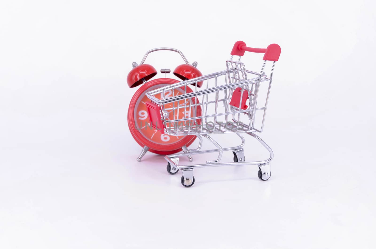 Shopping cart and classic alarm clock on white background. Sale time buy mall market shop consumer concept. Selective focus.