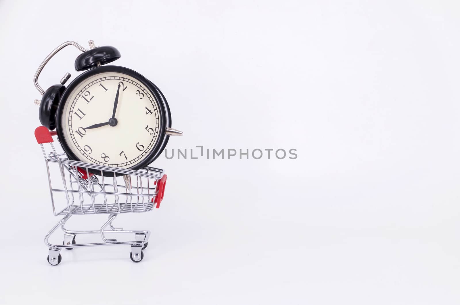 Shopping cart and classic alarm clock on white background. Sale time buy mall market shop consumer concept. Selective focus.