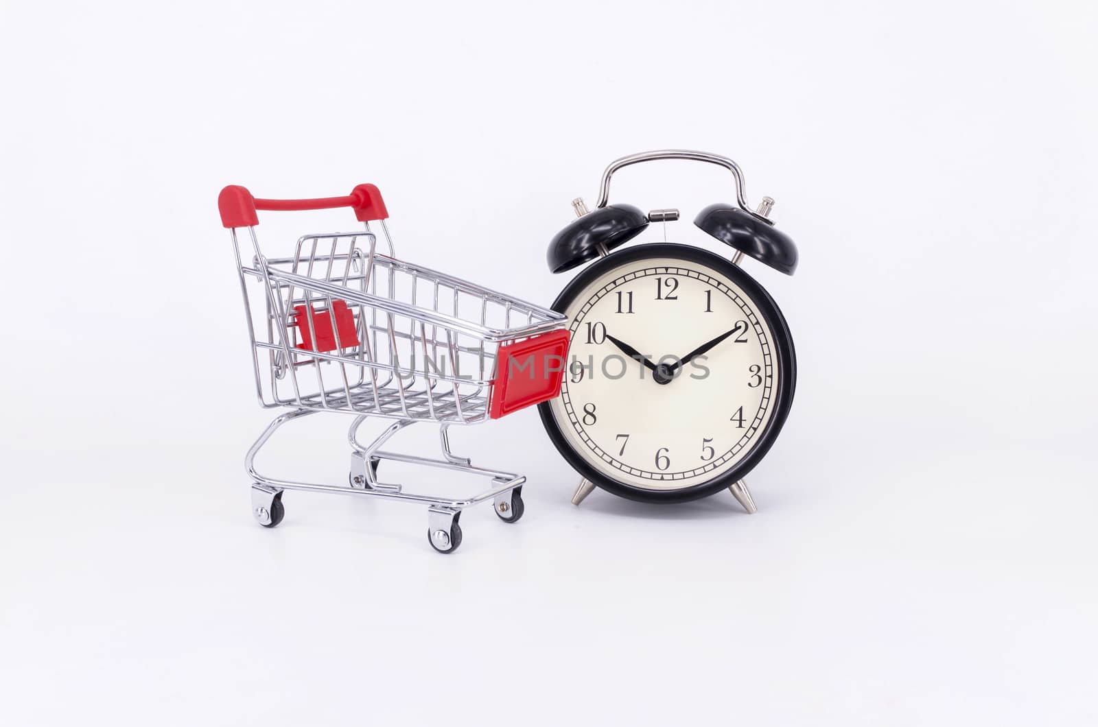 Shopping cart and classic alarm clock on white background. Sale time buy mall market shop consumer concept. Selective focus.