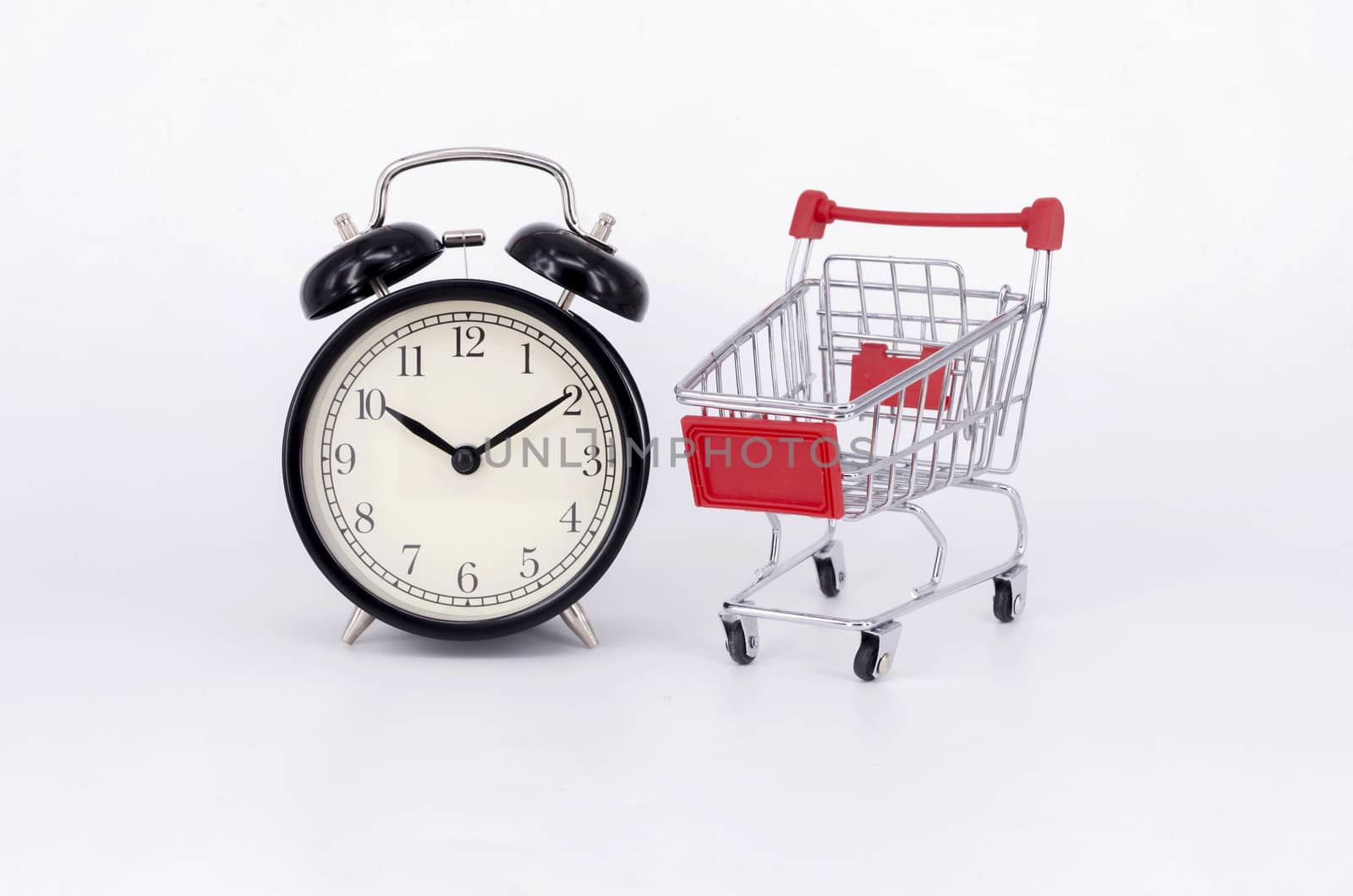 Shopping cart and classic alarm clock on white background. Sale time buy mall market shop consumer concept. Selective focus.