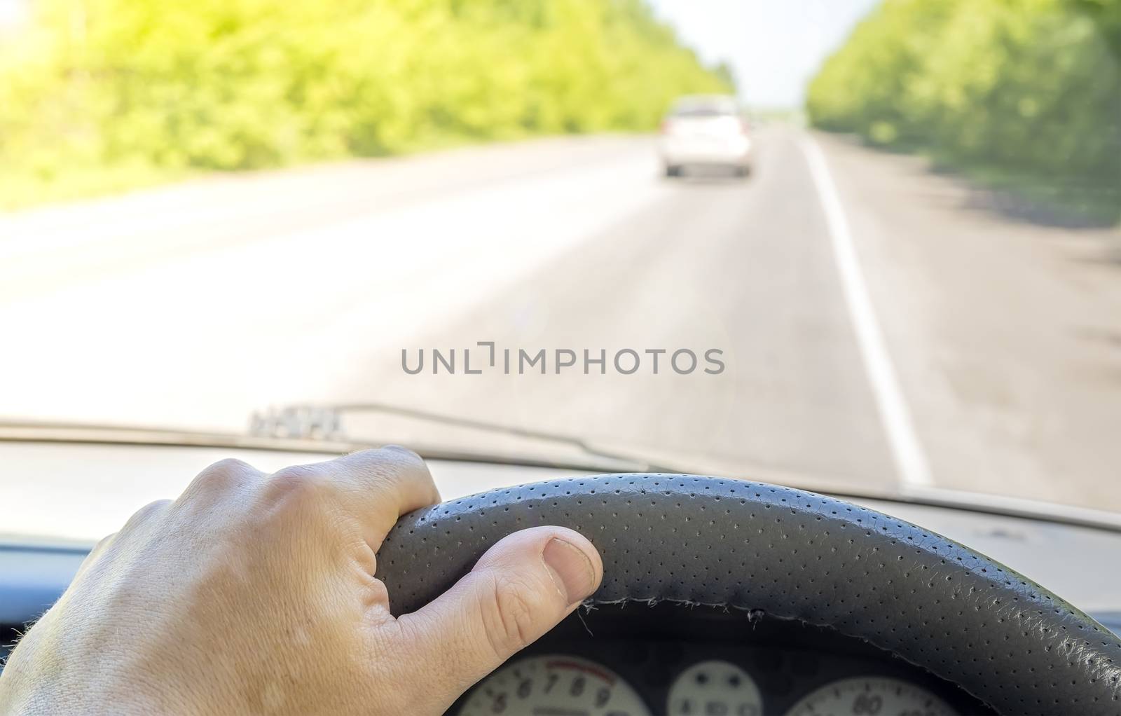 the driver hand on the steering wheel of a car that is passing on a country highway